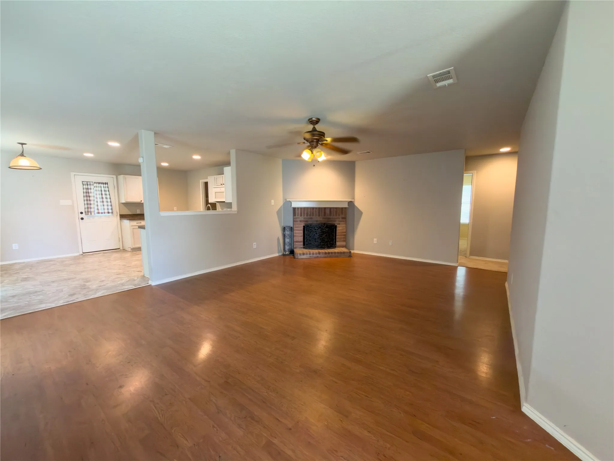 Spacious living area featuring wood-finish flooring, a brick fireplace, and a ceiling fan