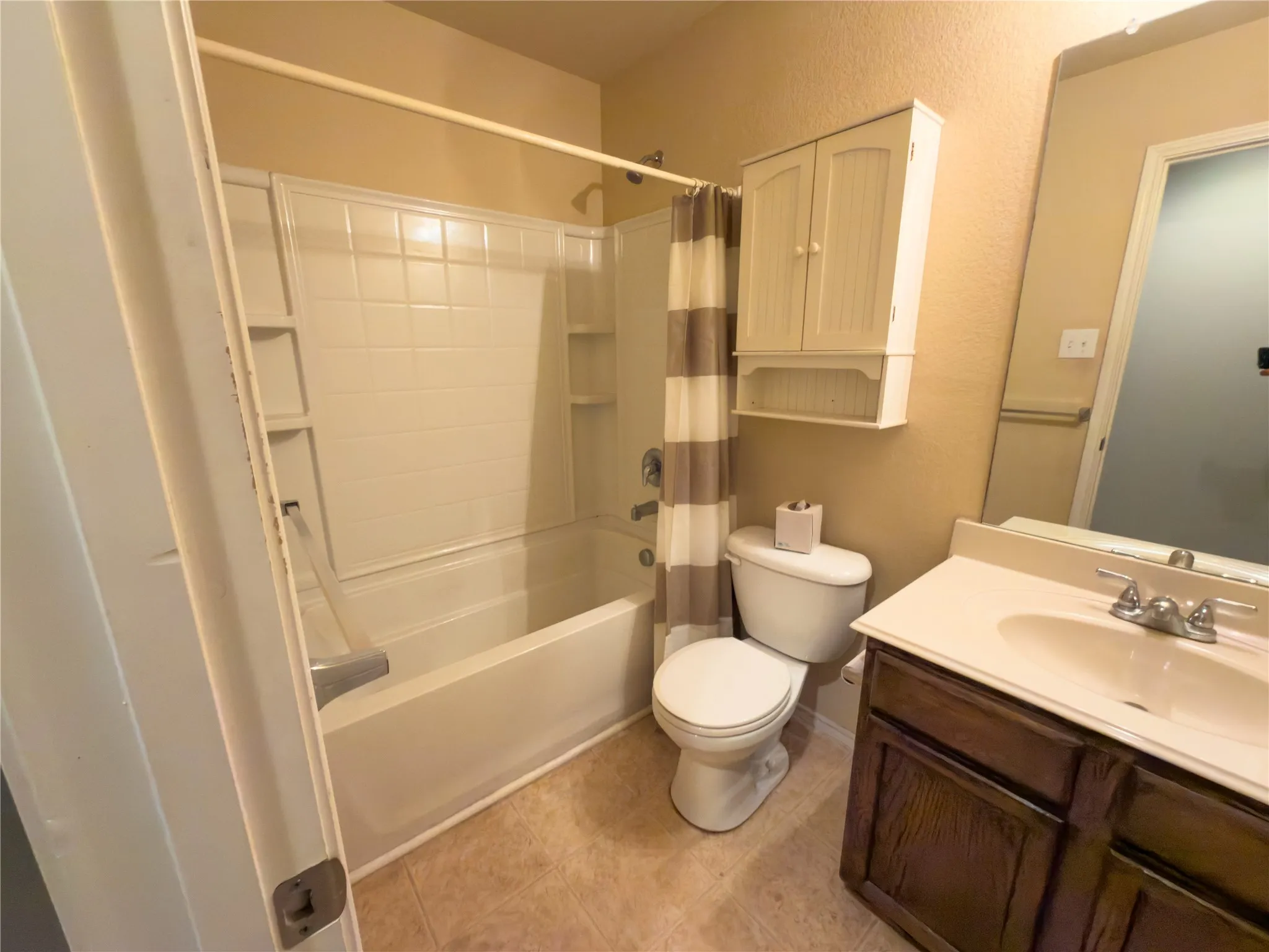 Bathroom featuring a shower-tub combination with white surround, a toilet, a wall-mounted storage cabinet, and a vanity with a white countertop and a dark wood-finish base