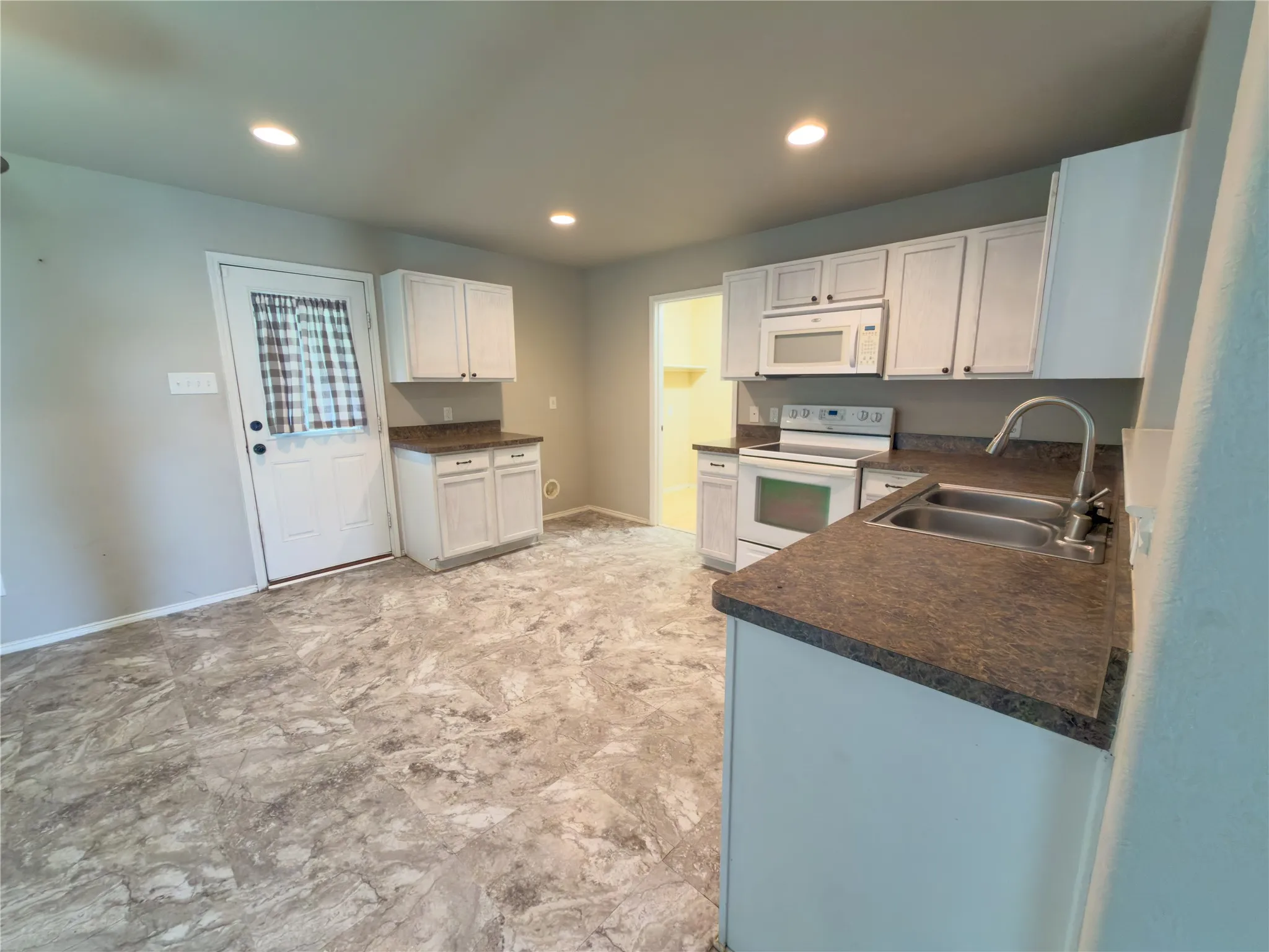 Kitchen featuring white cabinetry, dark countertops, a double basin stainless steel sink, and a white appliance suite including a range and microwave