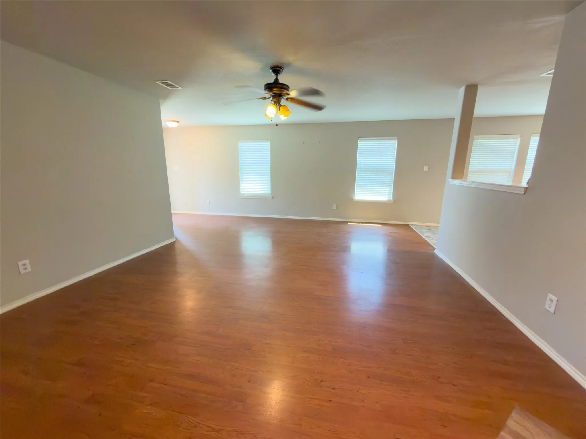 Spacious interior featuring wood-finish flooring, neutral paint palette, multiple windows with blinds, and a ceiling fan with integrated lighting