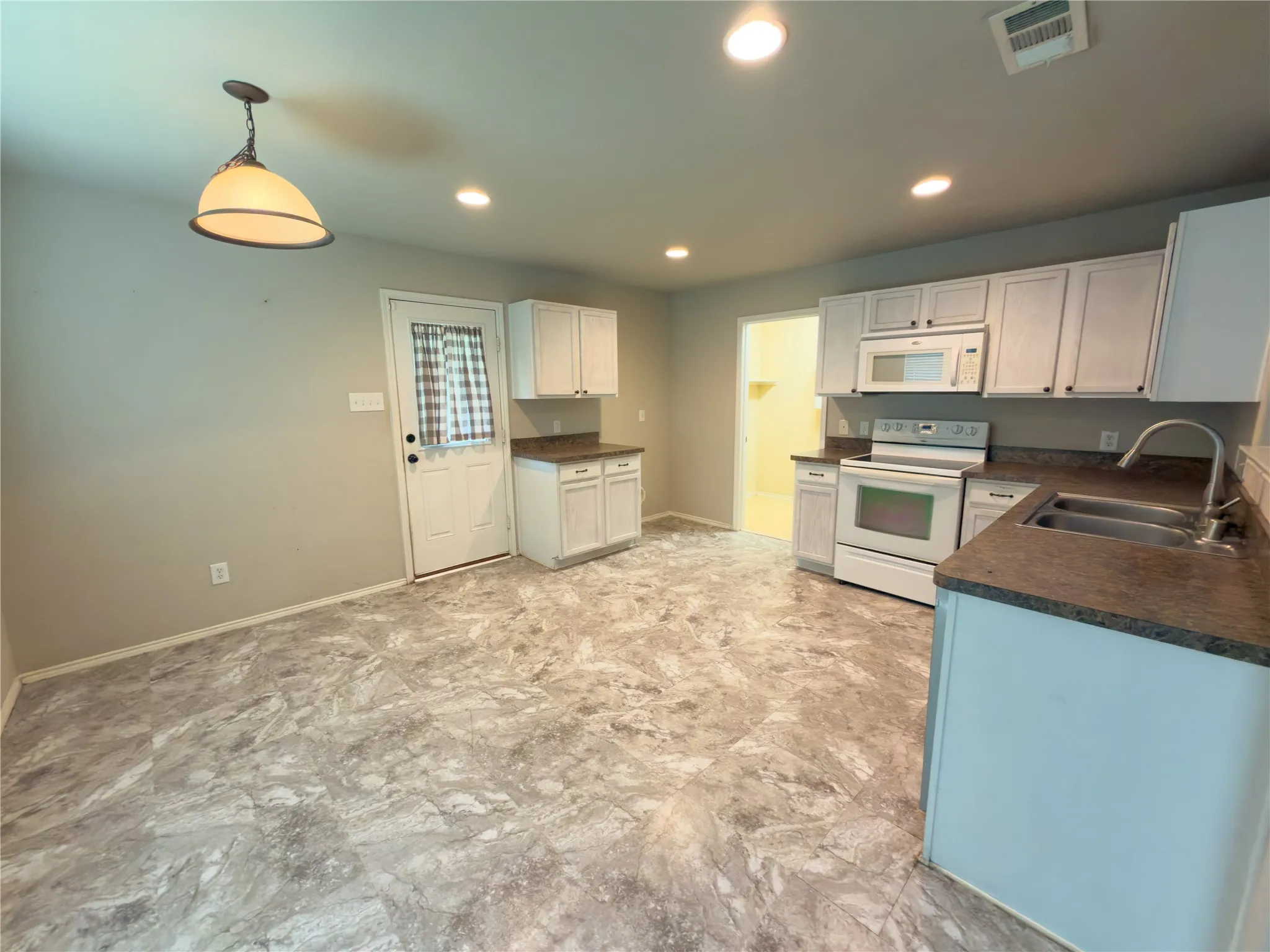 Kitchen featuring white cabinetry with dark hardware, dark countertops, and a double basin stainless steel sink