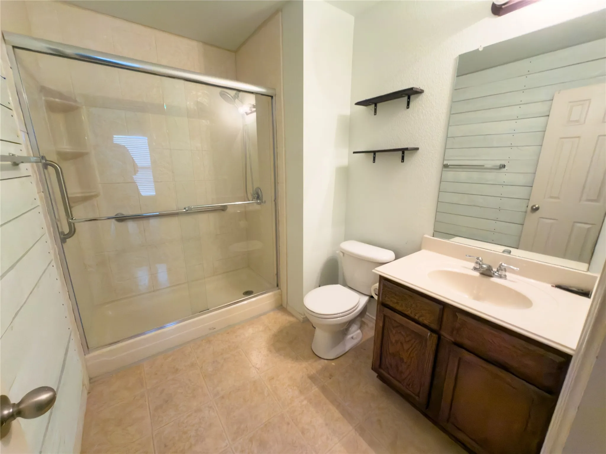 Full bathroom featuring a glass-enclosed shower with tile surround, a single vanity with wood-finish cabinetry and integrated sink, a toilet, and neutral tone flooring