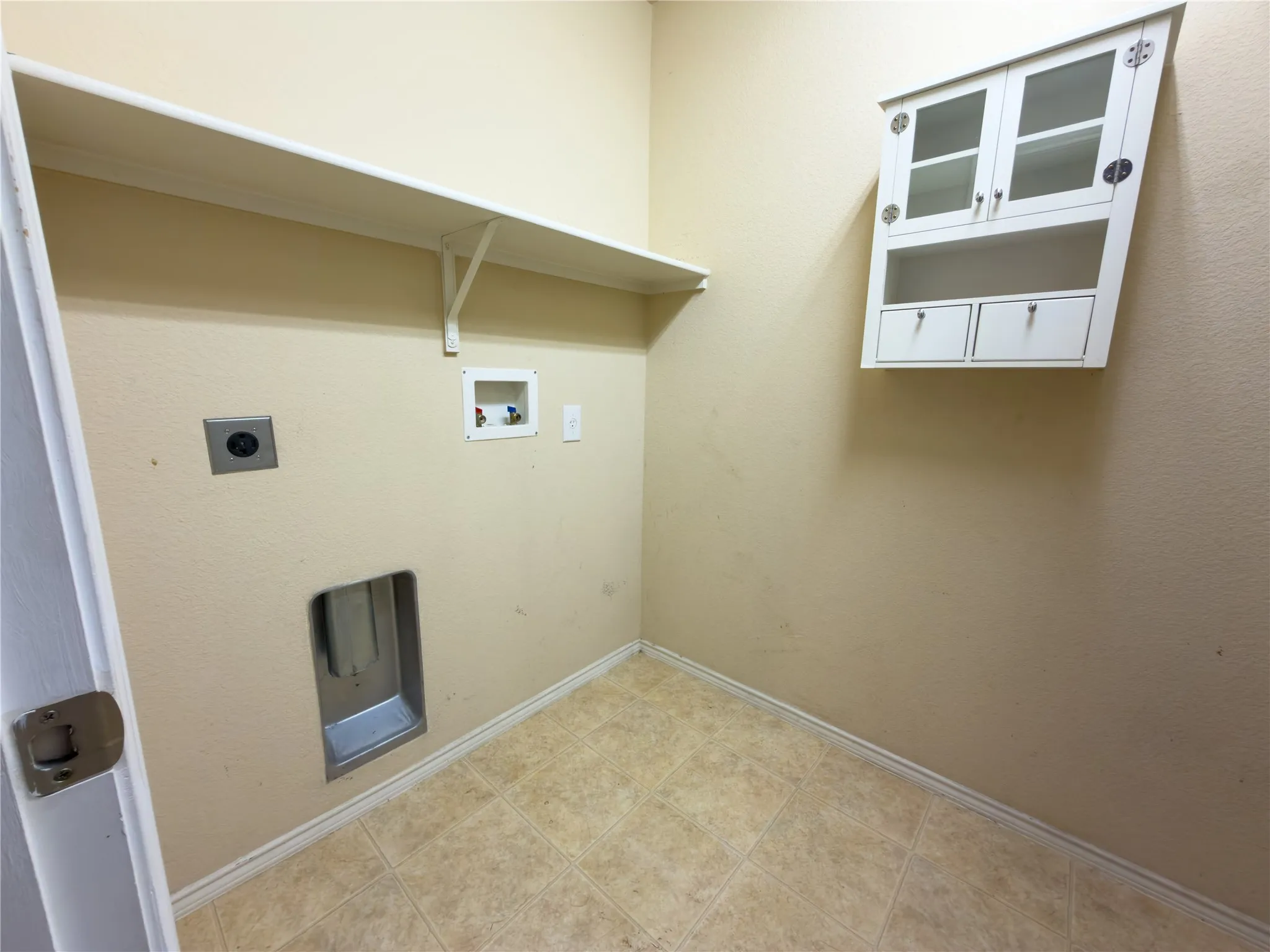 Dedicated laundry area featuring a white wall-mounted storage cabinet with glass-fronted doors and drawers, a white wall shelf, and square tile flooring