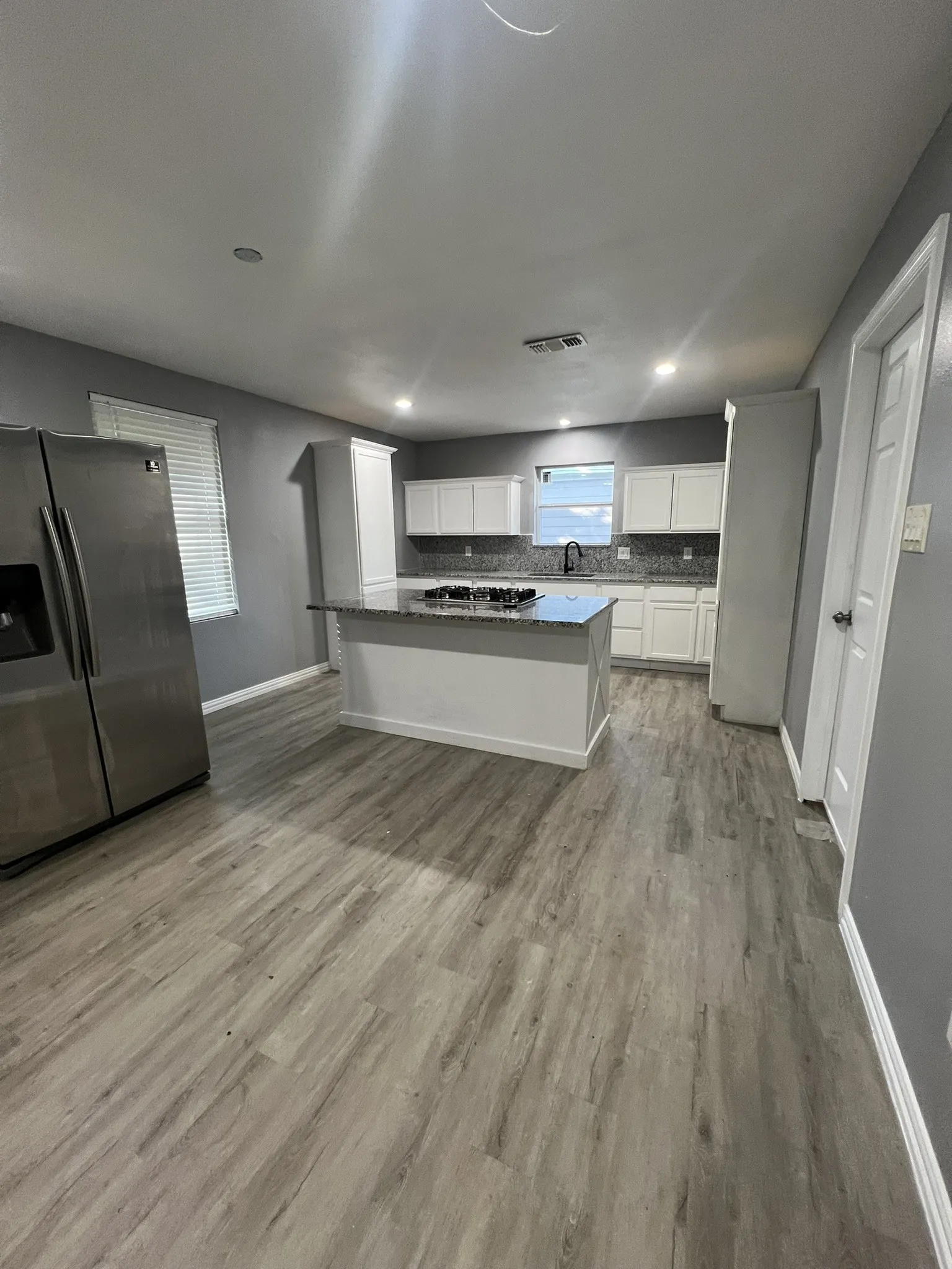 Kitchen featuring a central island with a granite-style countertop, white cabinetry, a tile backsplash, and recessed lighting
