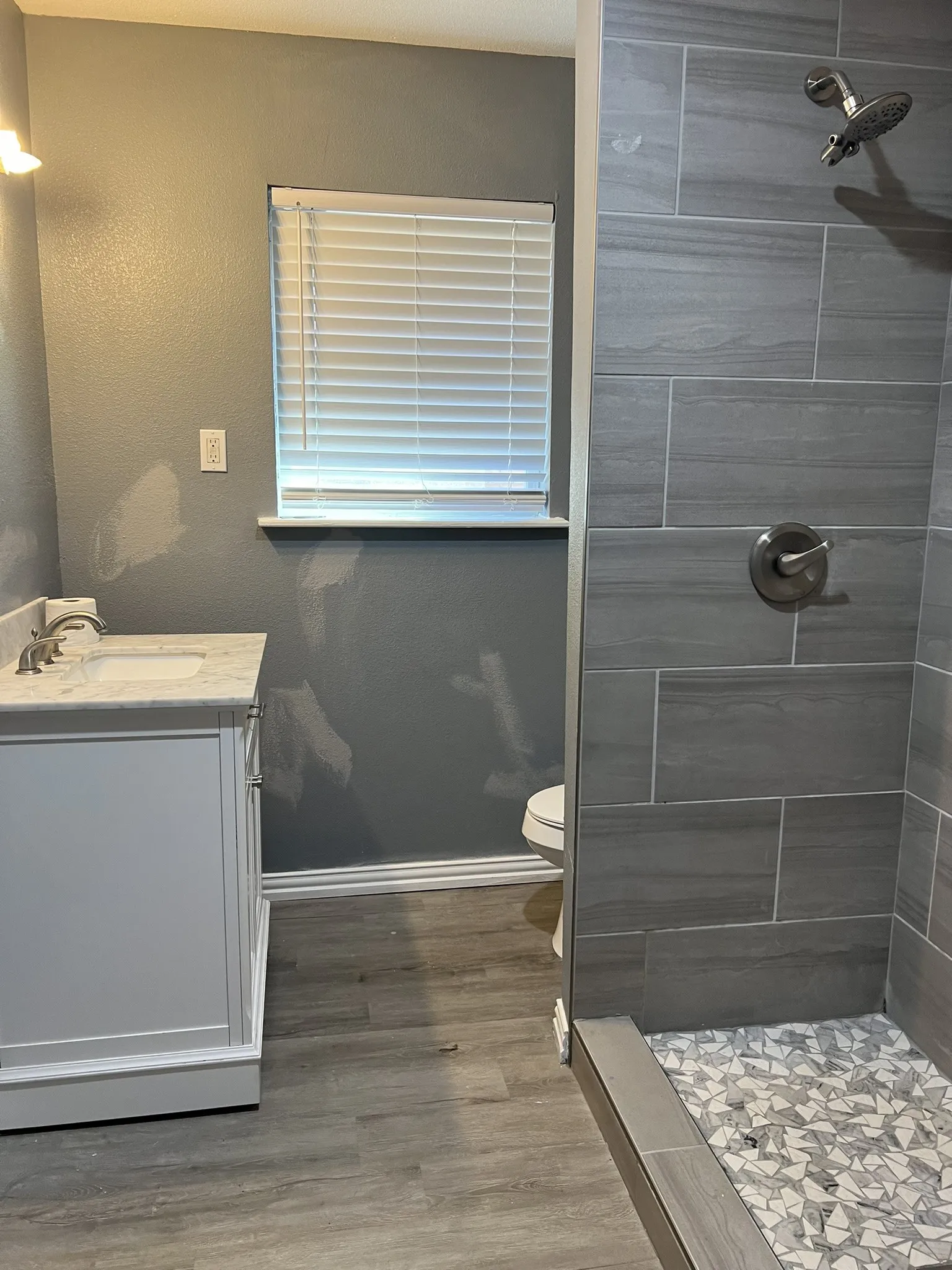 Modern bathroom featuring a tiled shower with mosaic floor, a single vanity with a white countertop and brushed nickel fixtures, and wood-finish flooring