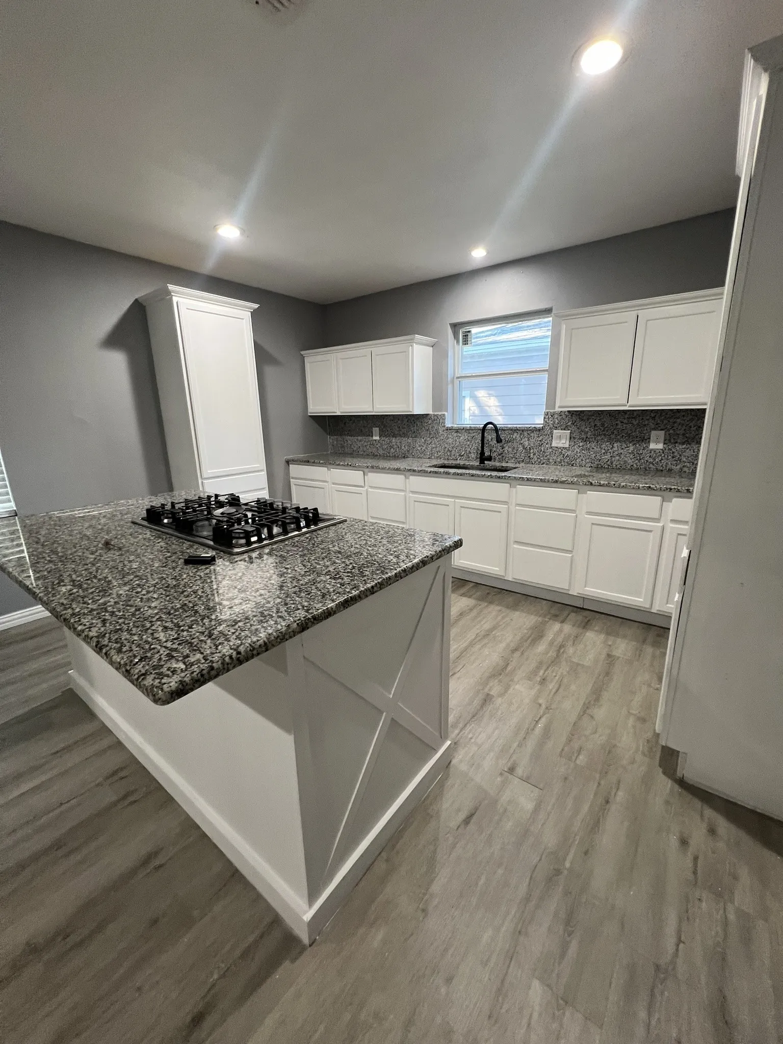 Kitchen featuring an island with a built-in cooktop, white cabinetry, granite countertops, and wood-finish flooring