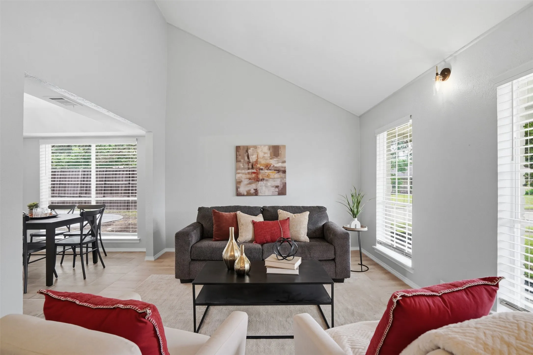 Vaulted ceilings define this living space featuring light wood-finish flooring and multiple windows with white blinds