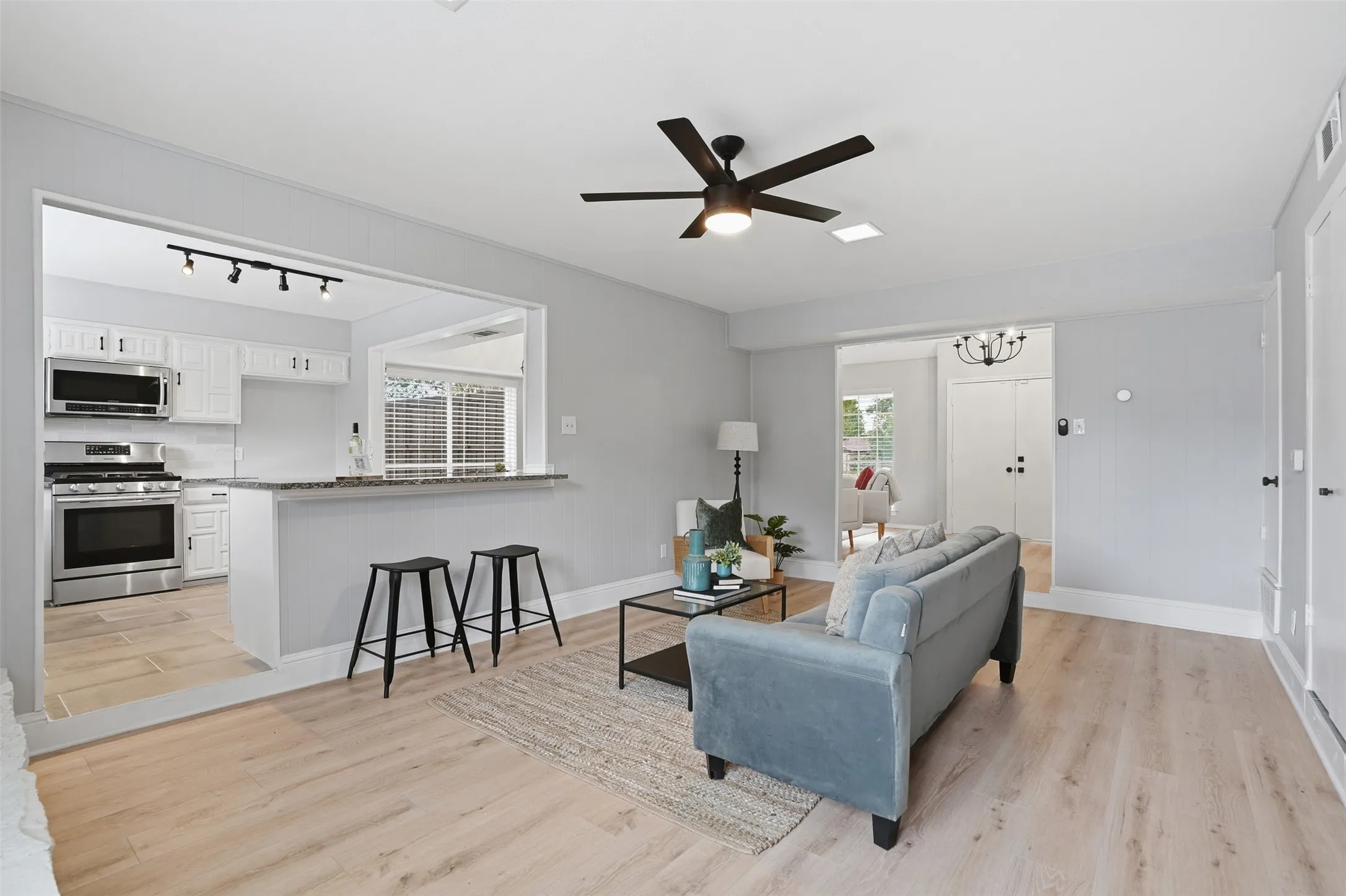 Open-concept living area featuring light wood-finish flooring, a modern black ceiling fan, and recessed lighting