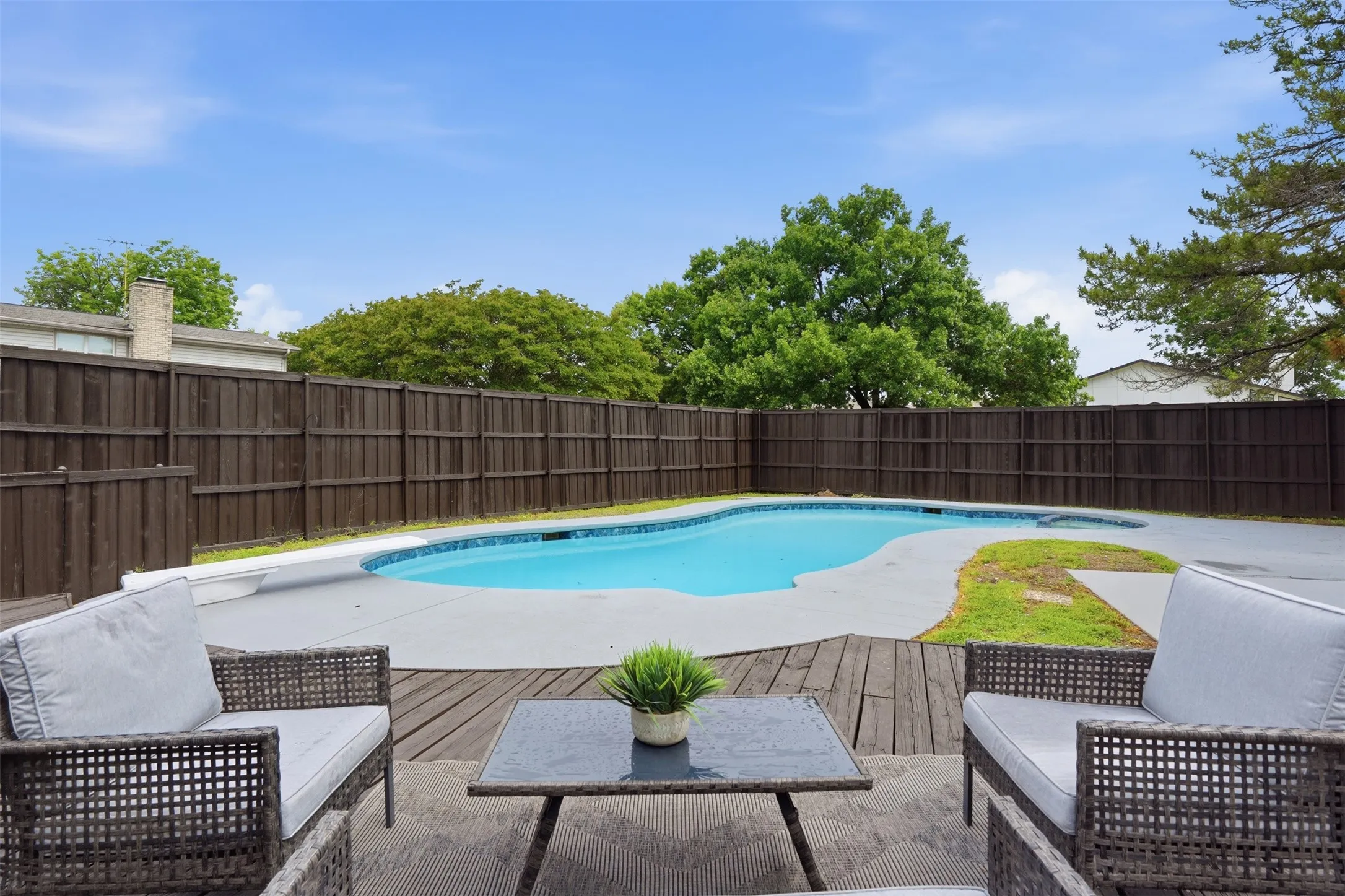 Outdoor oasis featuring a freeform swimming pool with concrete decking, surrounded by a privacy fence and mature trees