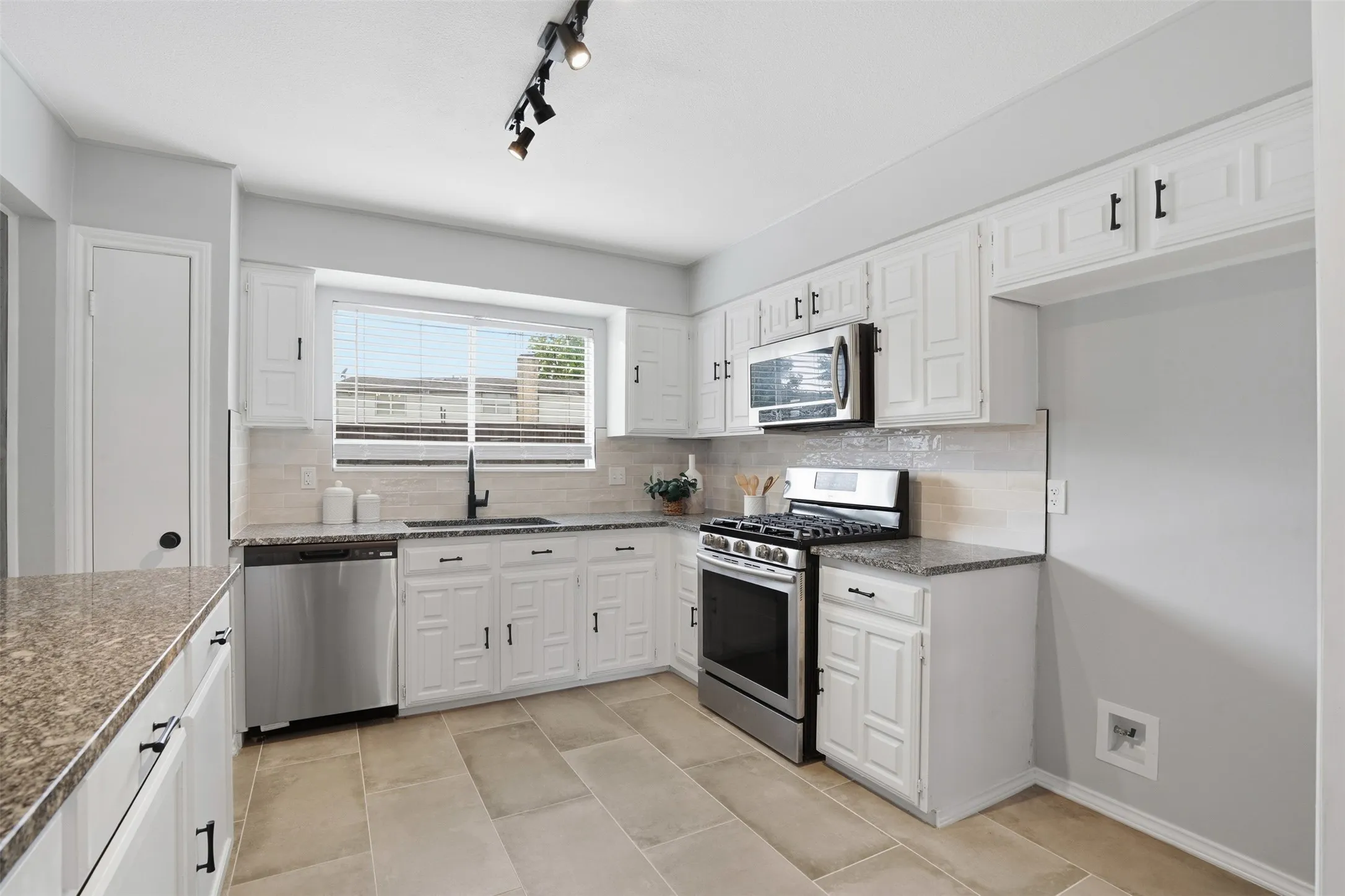 Well-appointed kitchen featuring white cabinetry, granite countertops, stainless steel appliances, a tile backsplash, and large format tile flooring