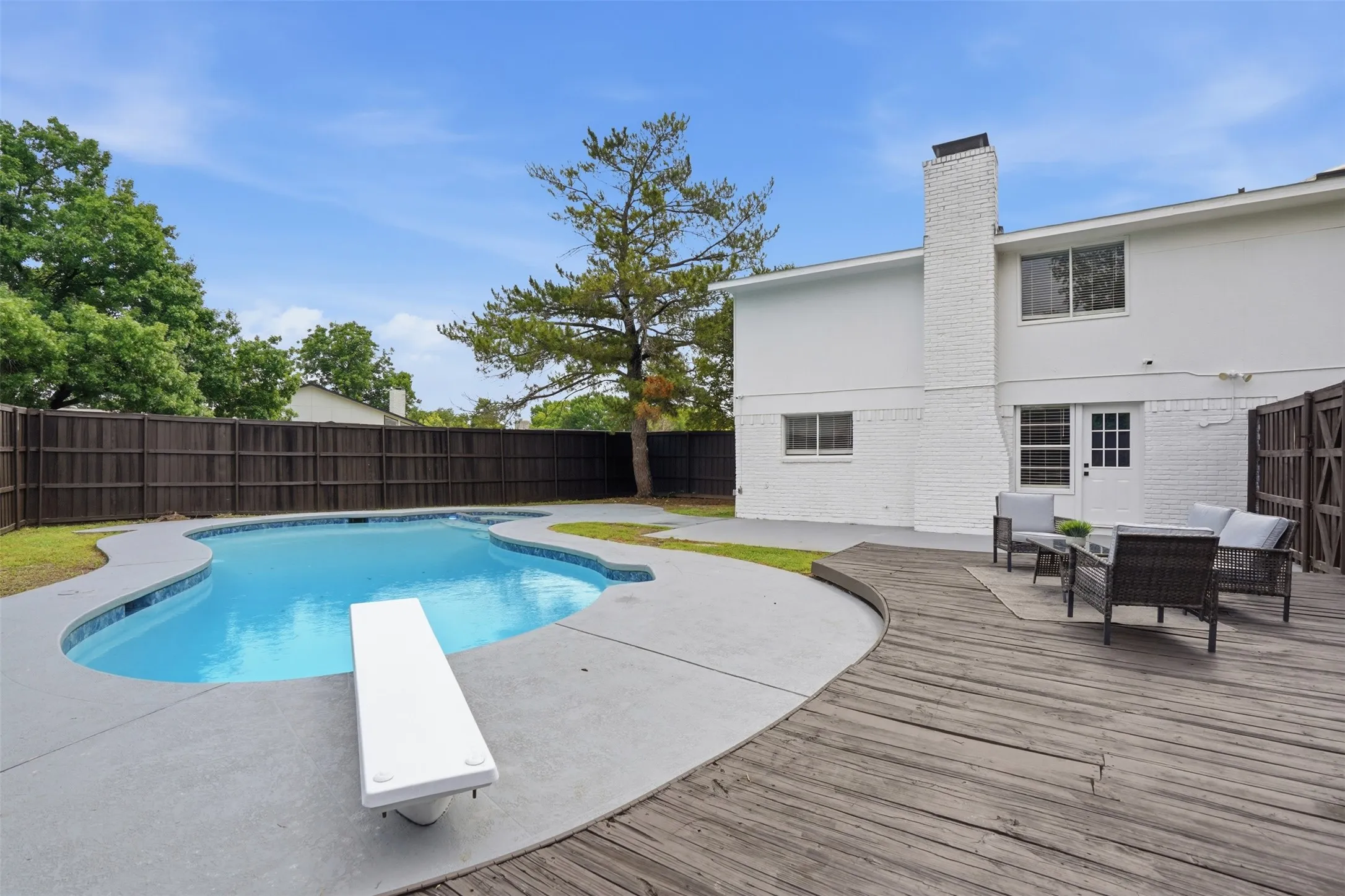 Expansive backyard featuring a custom-shaped swimming pool with a diving board, a surrounding concrete patio, and a spacious wood-finish deck