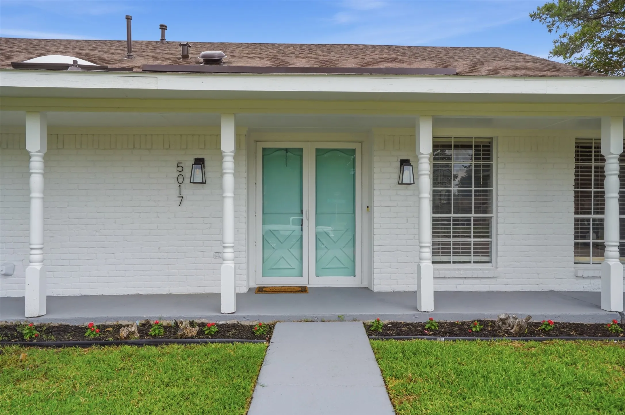 White brick exterior featuring a covered porch with decorative columns, a screened teal front door, and a paved walkway
