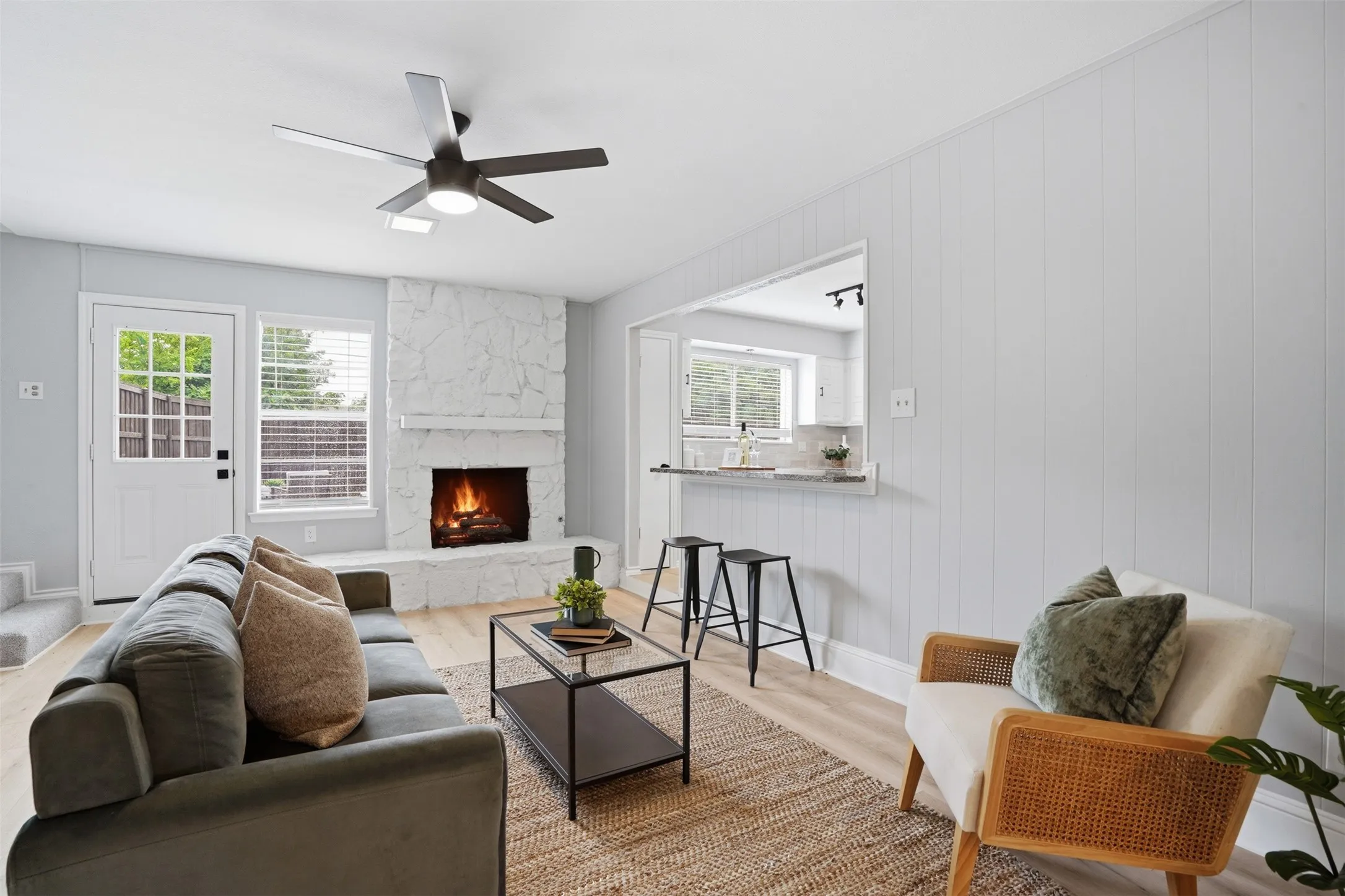 Living area featuring a stone fireplace with a white mantel, wood-finish flooring, and white vertical paneled walls