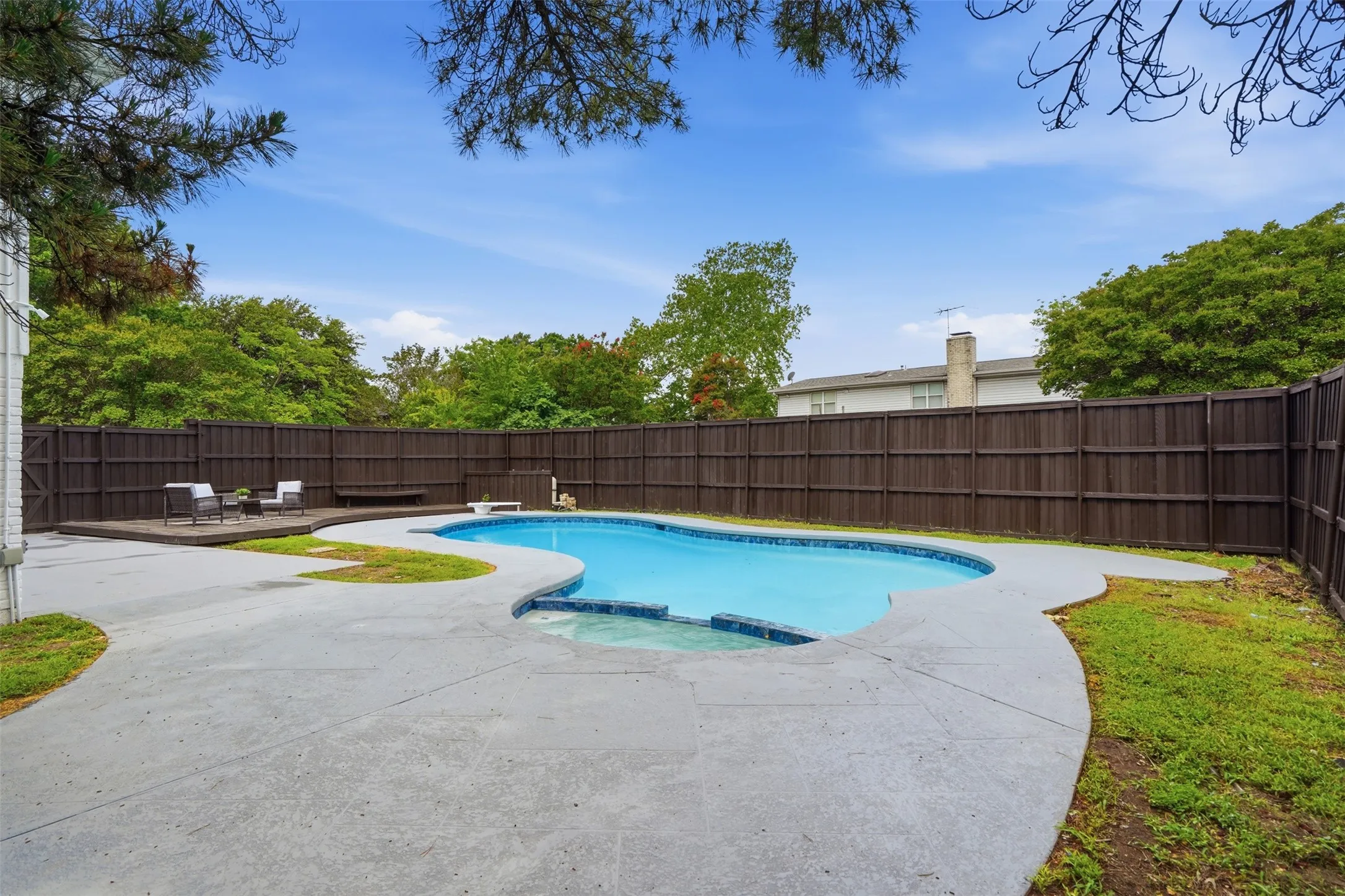 Outdoor living area featuring a freeform swimming pool with integrated spa, expansive concrete decking, and a separate wood-finish deck