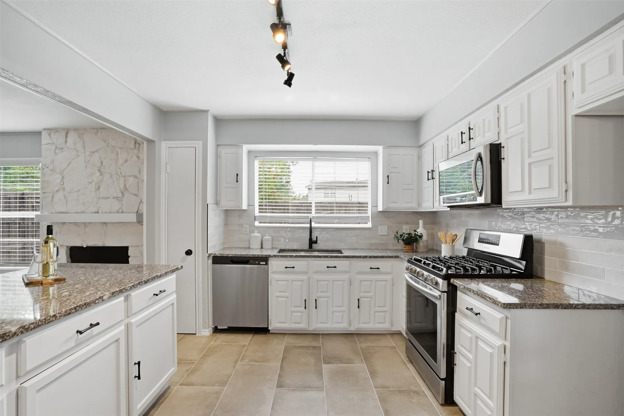 Kitchen featuring white cabinetry, stone countertops, stainless steel appliances, tile backsplash, and track lighting