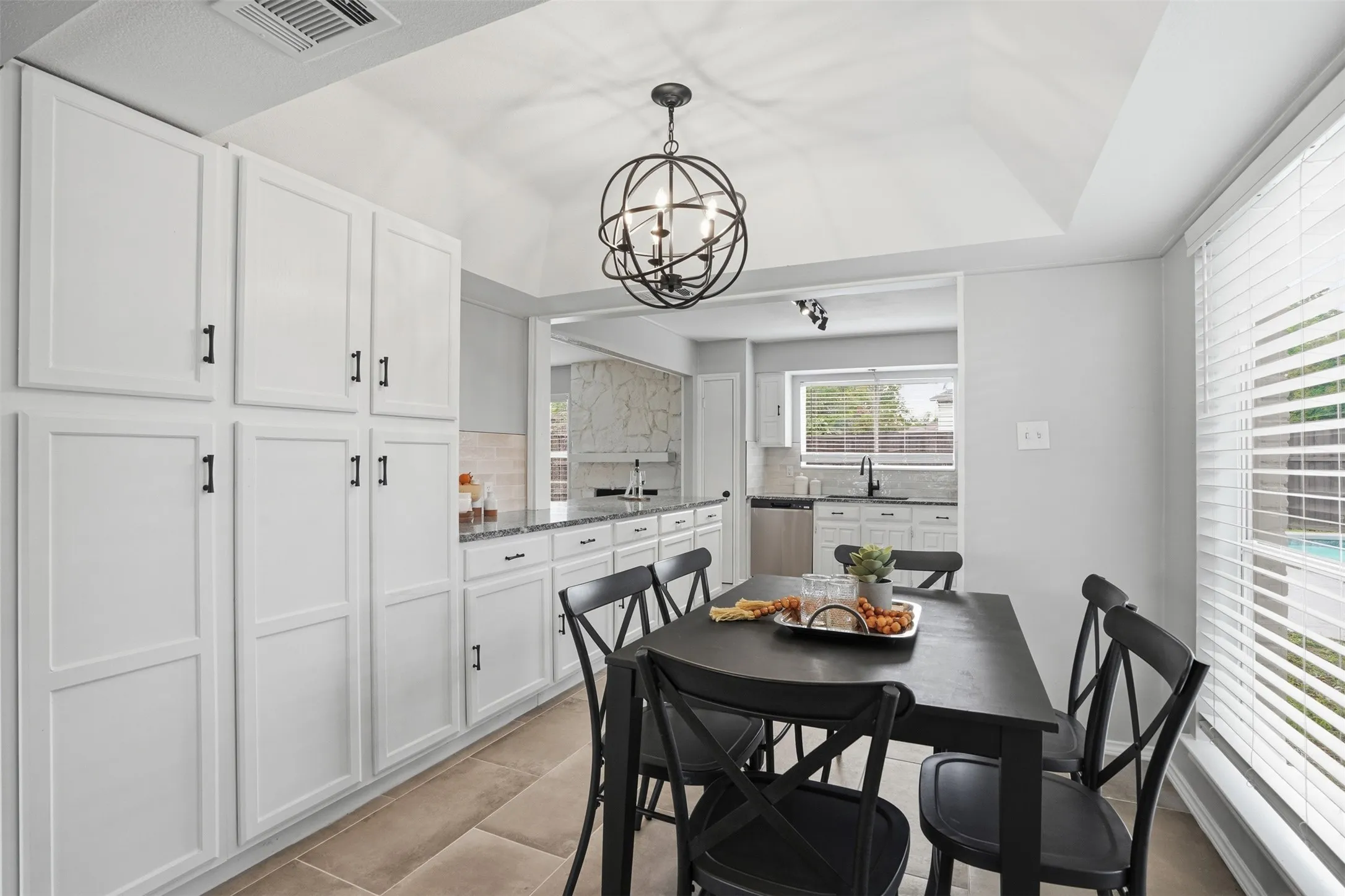 Dining area with vaulted ceilings, featuring an ornate black chandelier, extensive white cabinetry with black hardware, and tile flooring