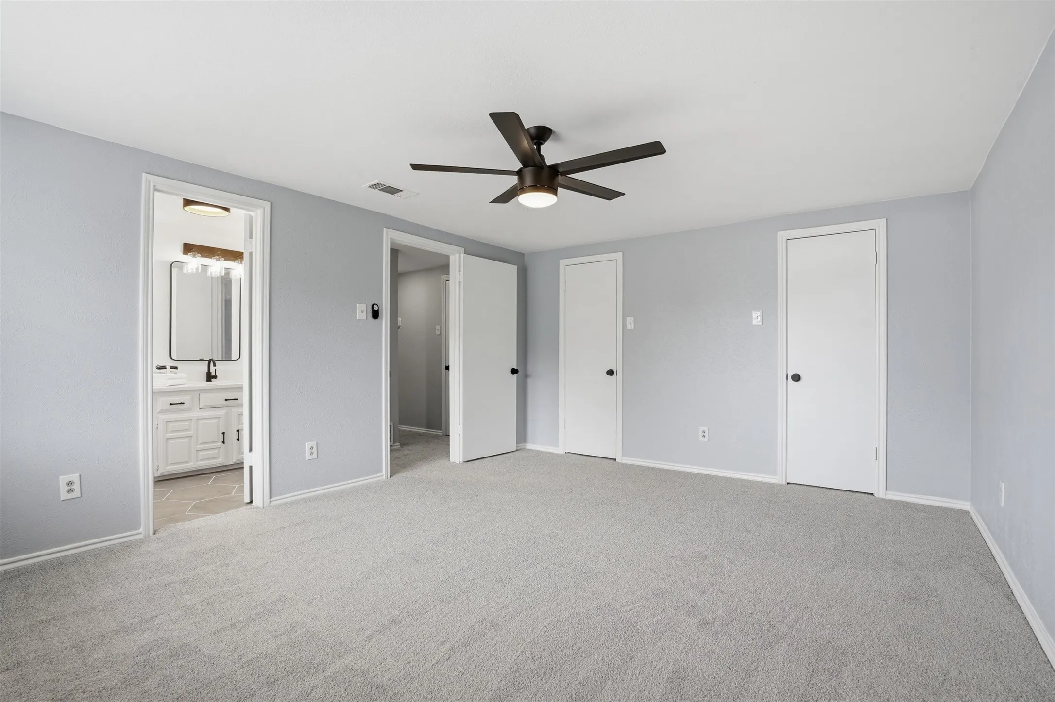 Spacious room featuring light gray walls, gray carpet flooring, and a contemporary ceiling fan with integrated lighting