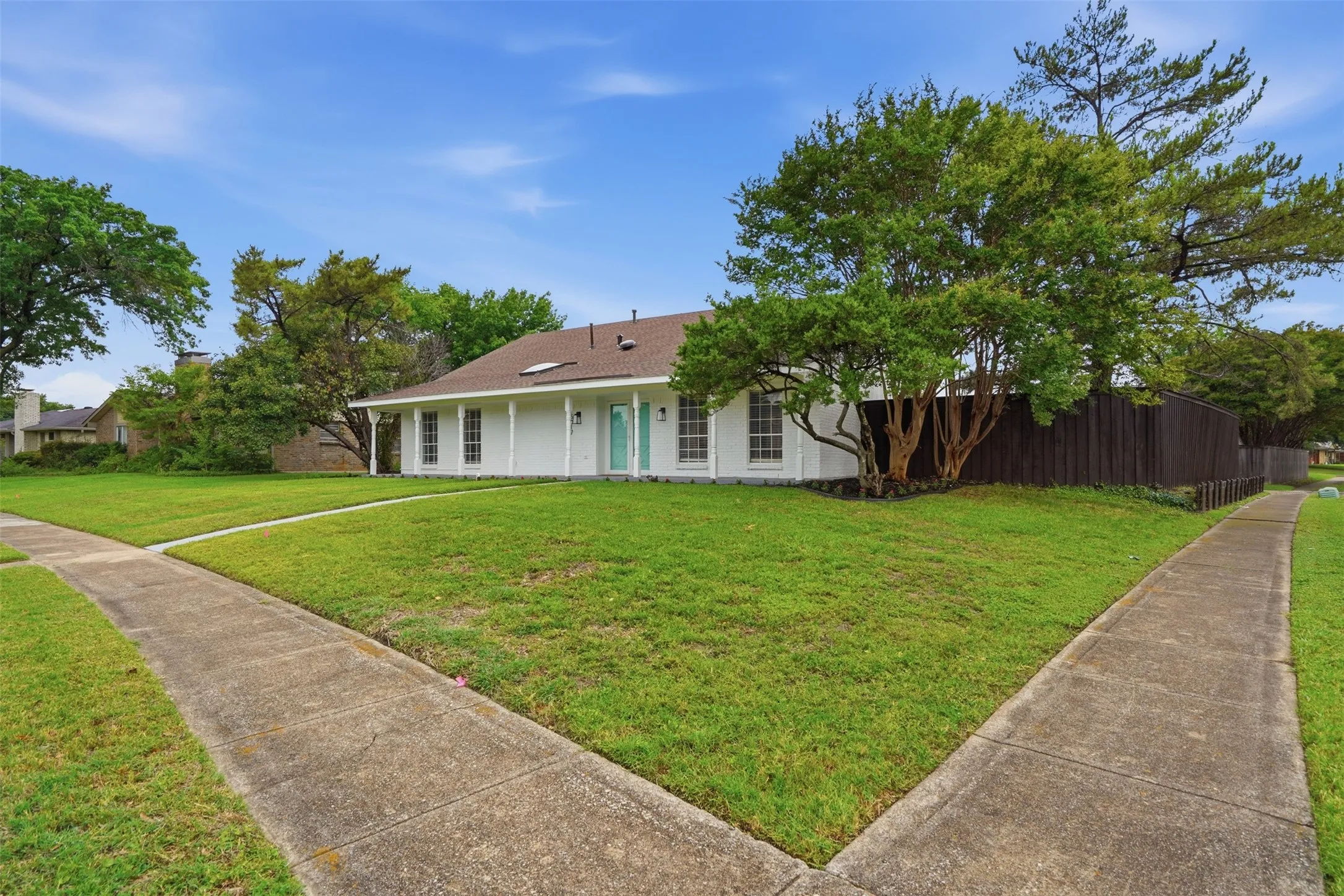 White single-story ranch-style residence featuring a brown shingle roof, twin skylights, and a turquoise front door