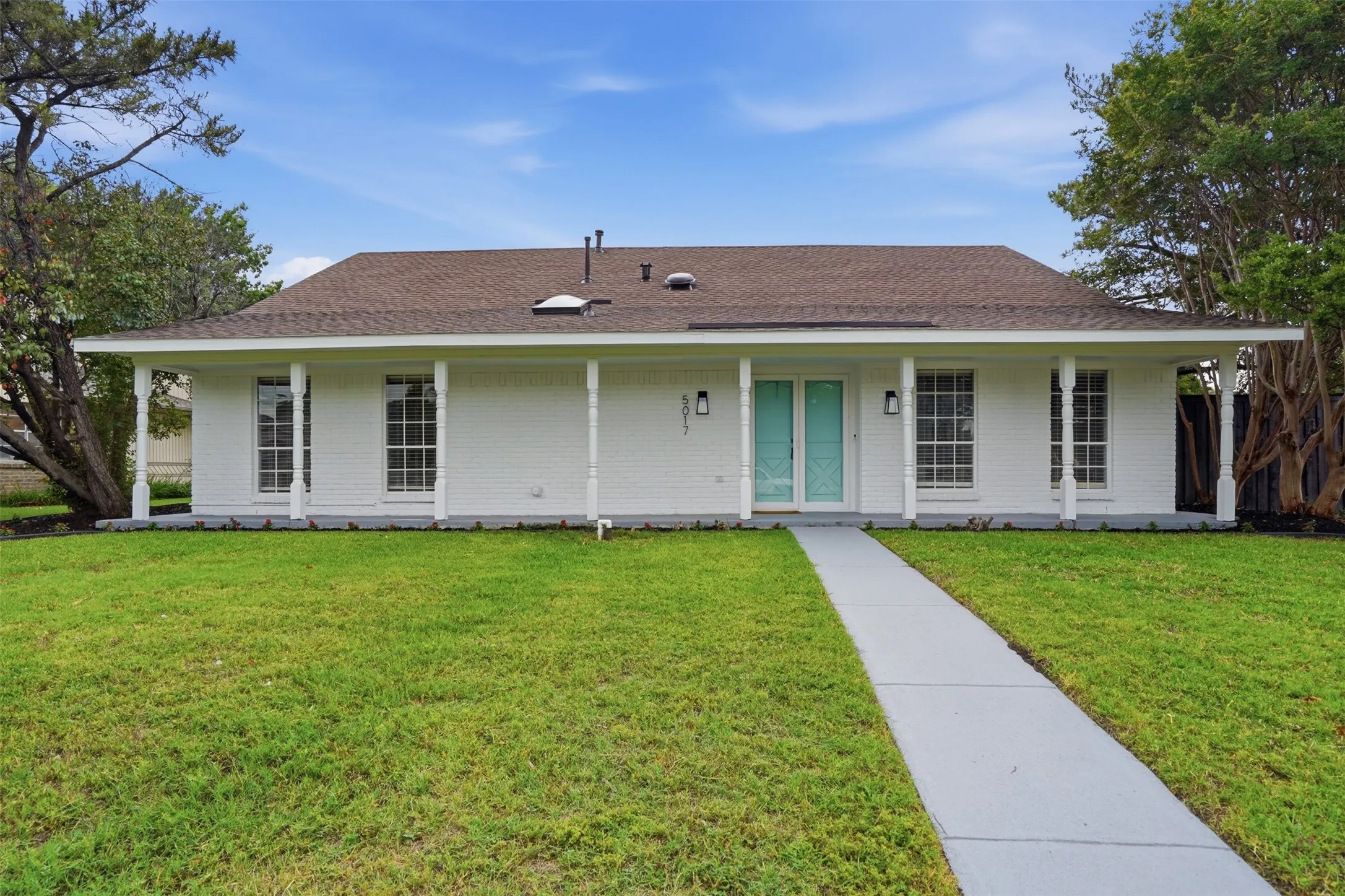 White brick residence featuring a full-width covered porch with white columns, a brown shingle roof, and a turquoise double entry door