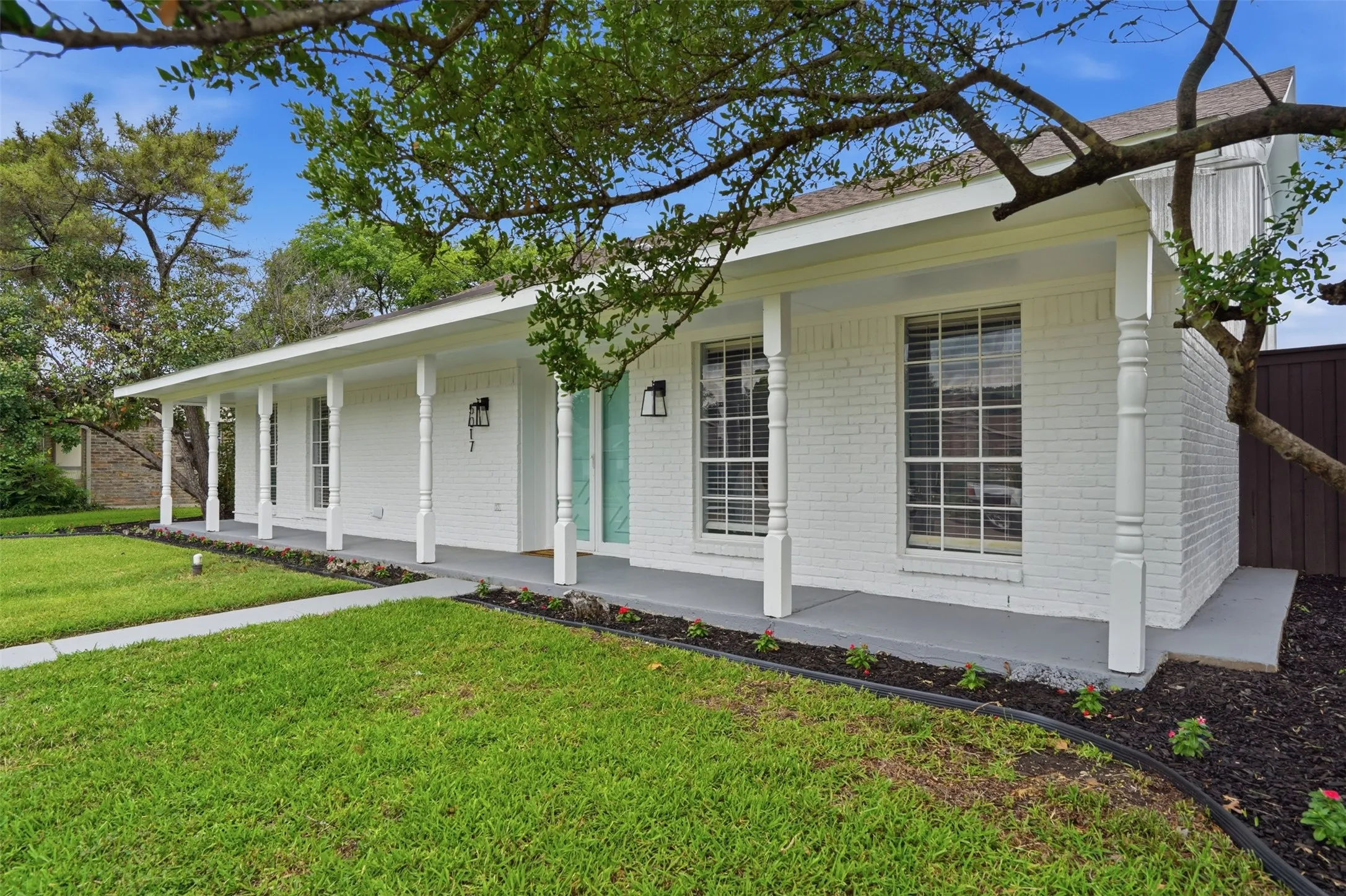 White brick exterior with a covered front porch featuring turned columns, a light blue front entry, and black exterior light fixtures