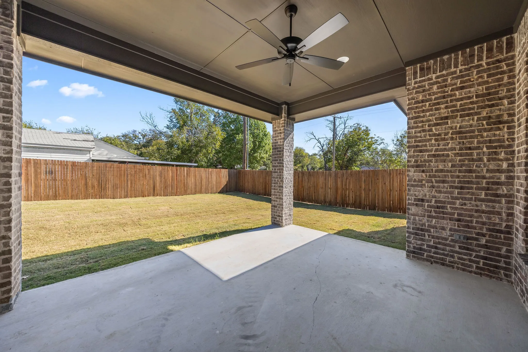 Covered patio with a ceiling fan, concrete flooring, and brick support columns