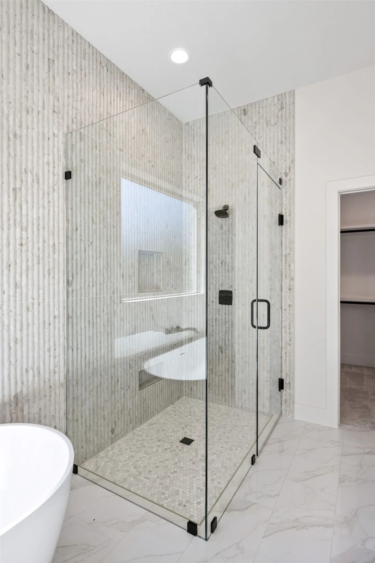Glass-enclosed shower with matte black fixtures, integrated bench, and mosaic tile flooring