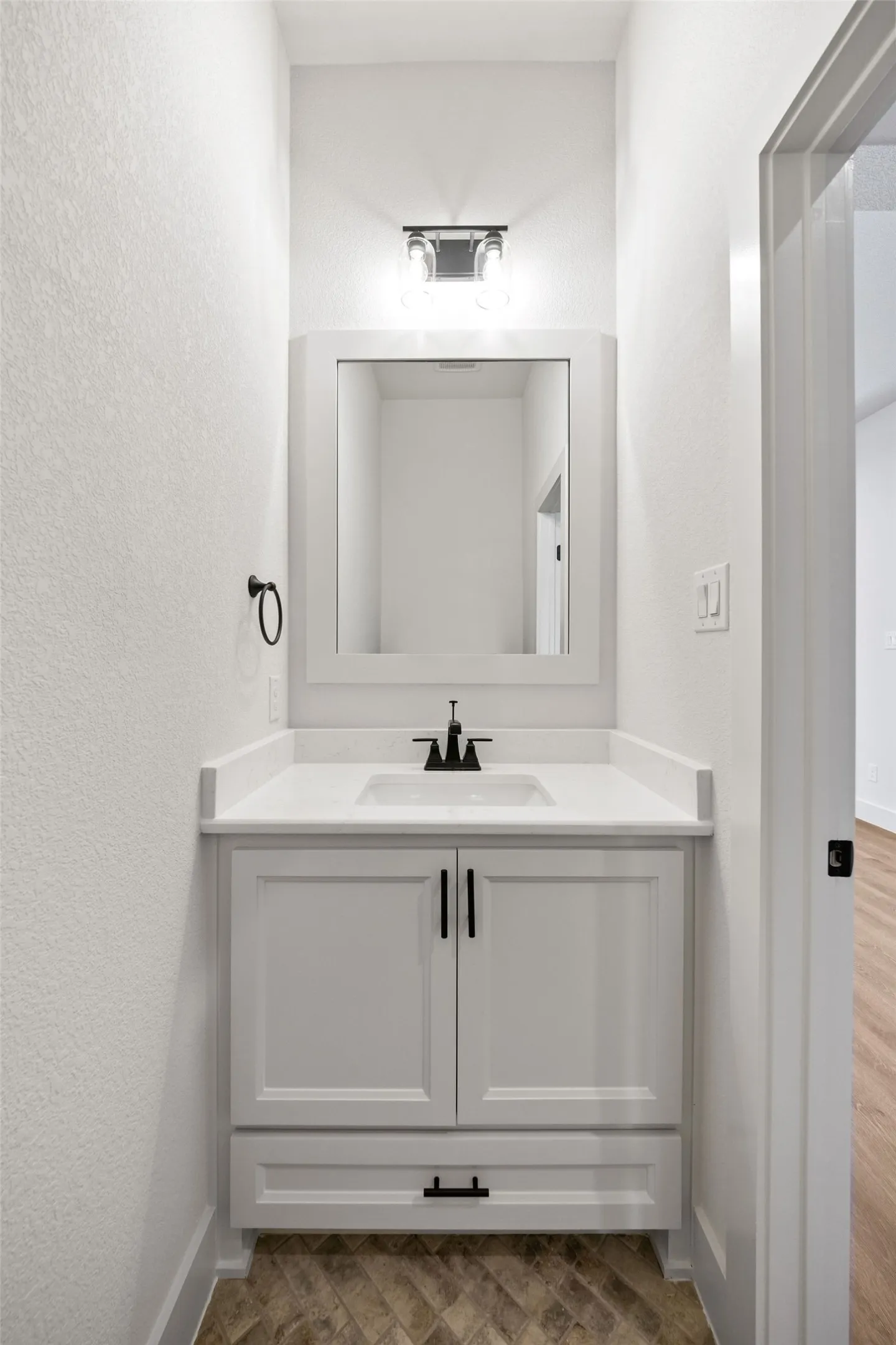 Vanity area featuring a framed mirror, white cabinetry, integrated sink, and matte black fixtures