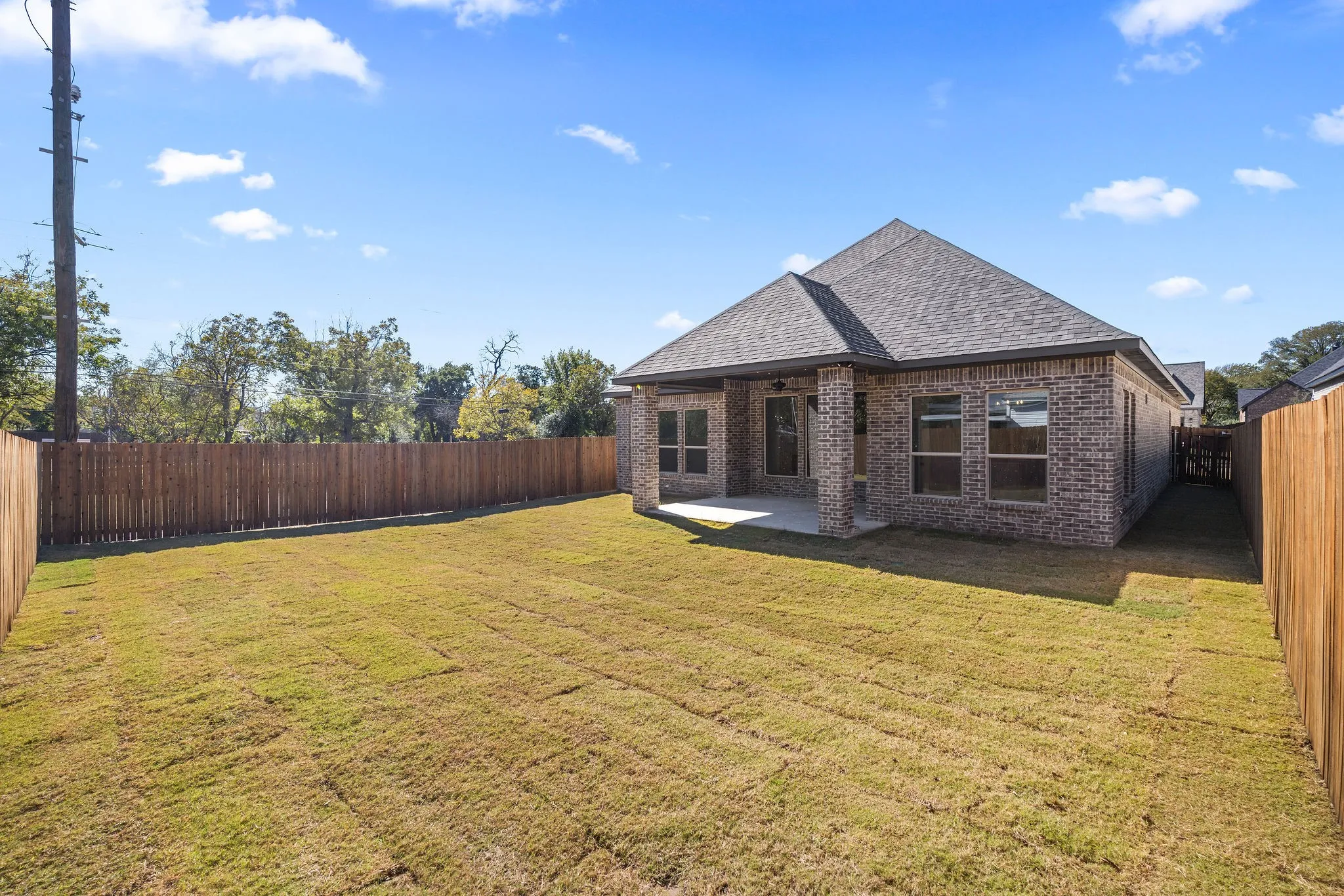 Spacious backyard with a wood privacy fence, sodded lawn, and a covered concrete patio