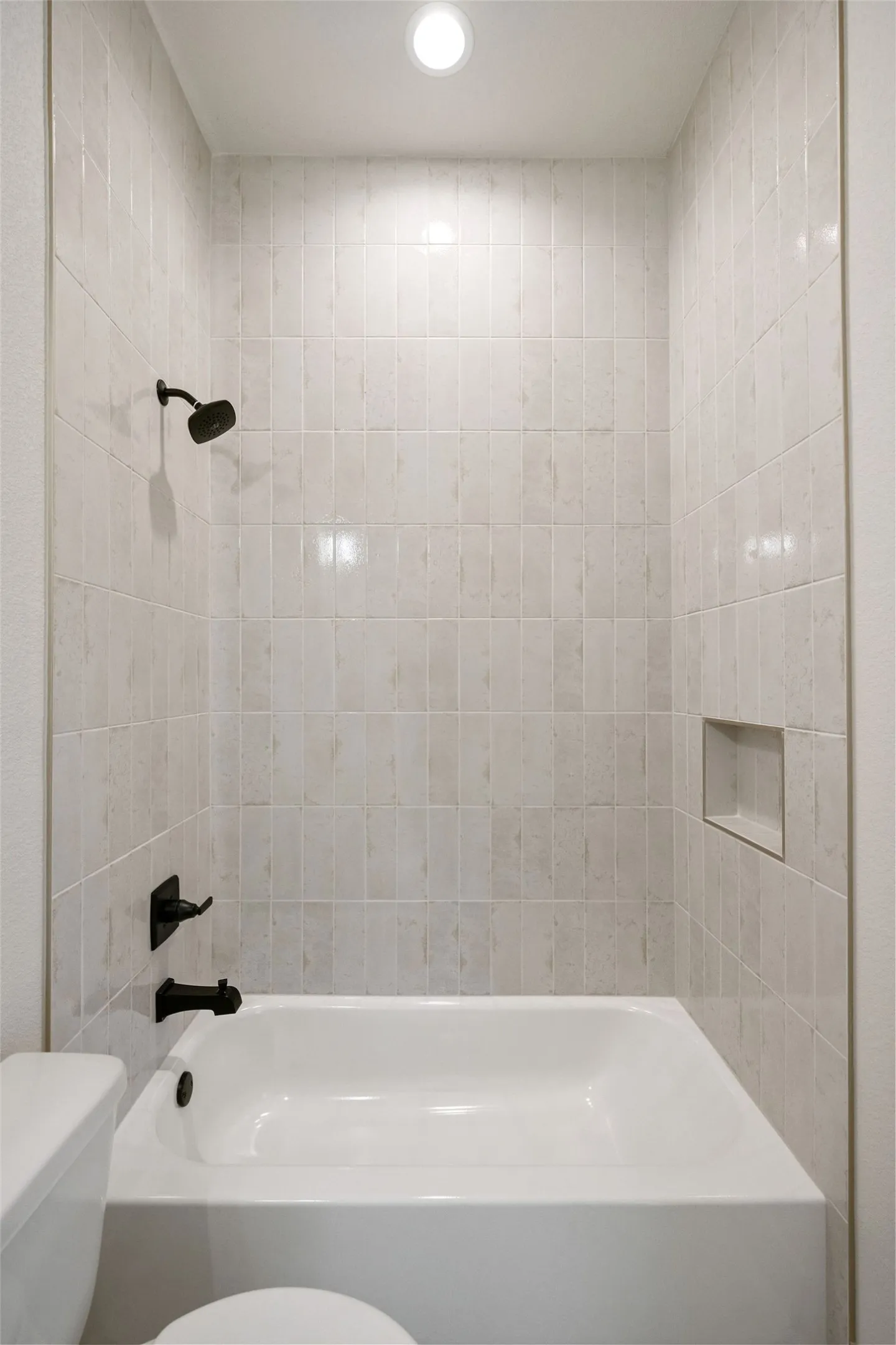 Bathtub and shower combination featuring floor-to-ceiling rectangular tile surround, matte black fixtures, an integrated shower niche, and a recessed ceiling light