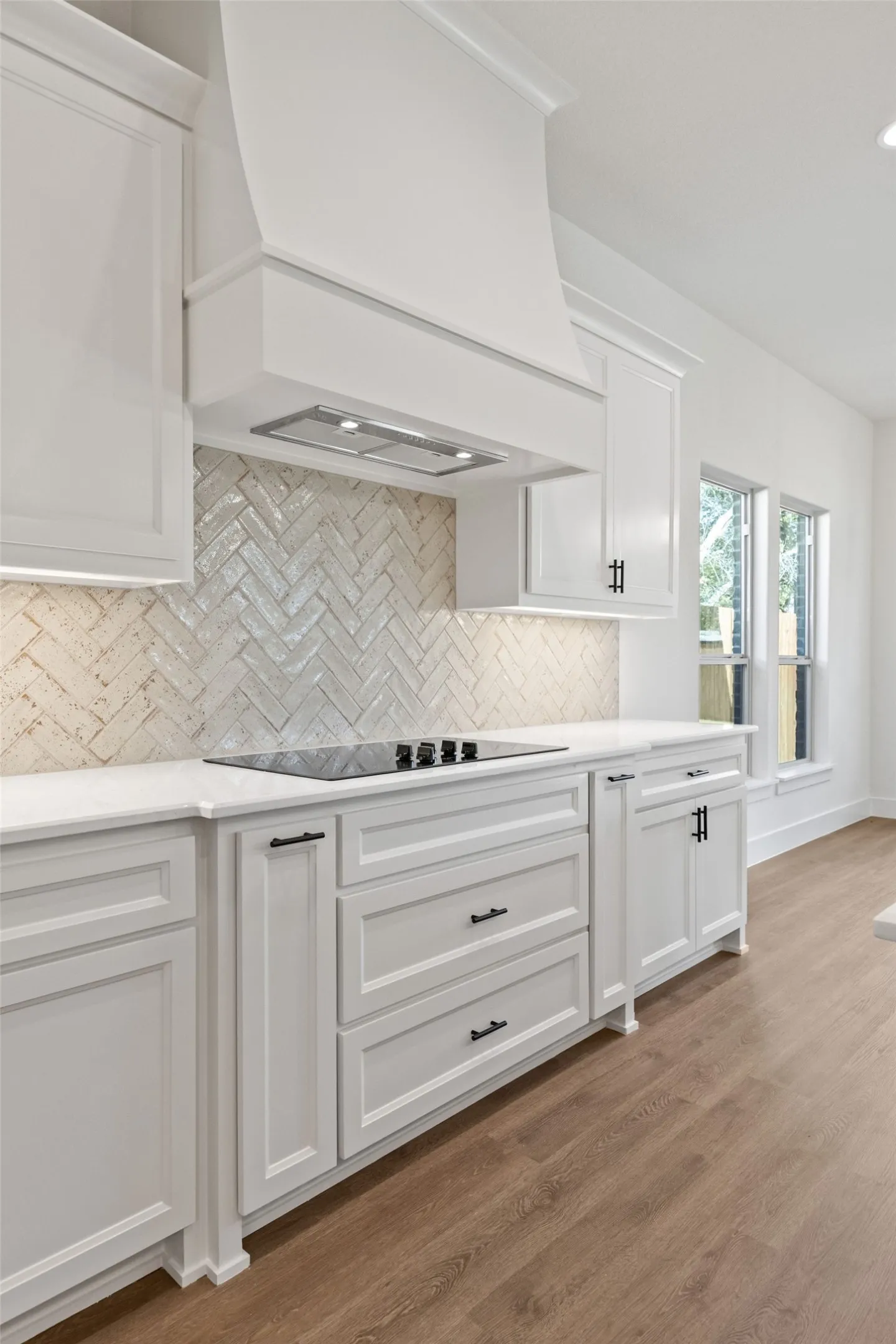 Contemporary kitchen showcasing white cabinetry, a built-in cooktop, white countertops, and a herringbone-patterned tile backsplash