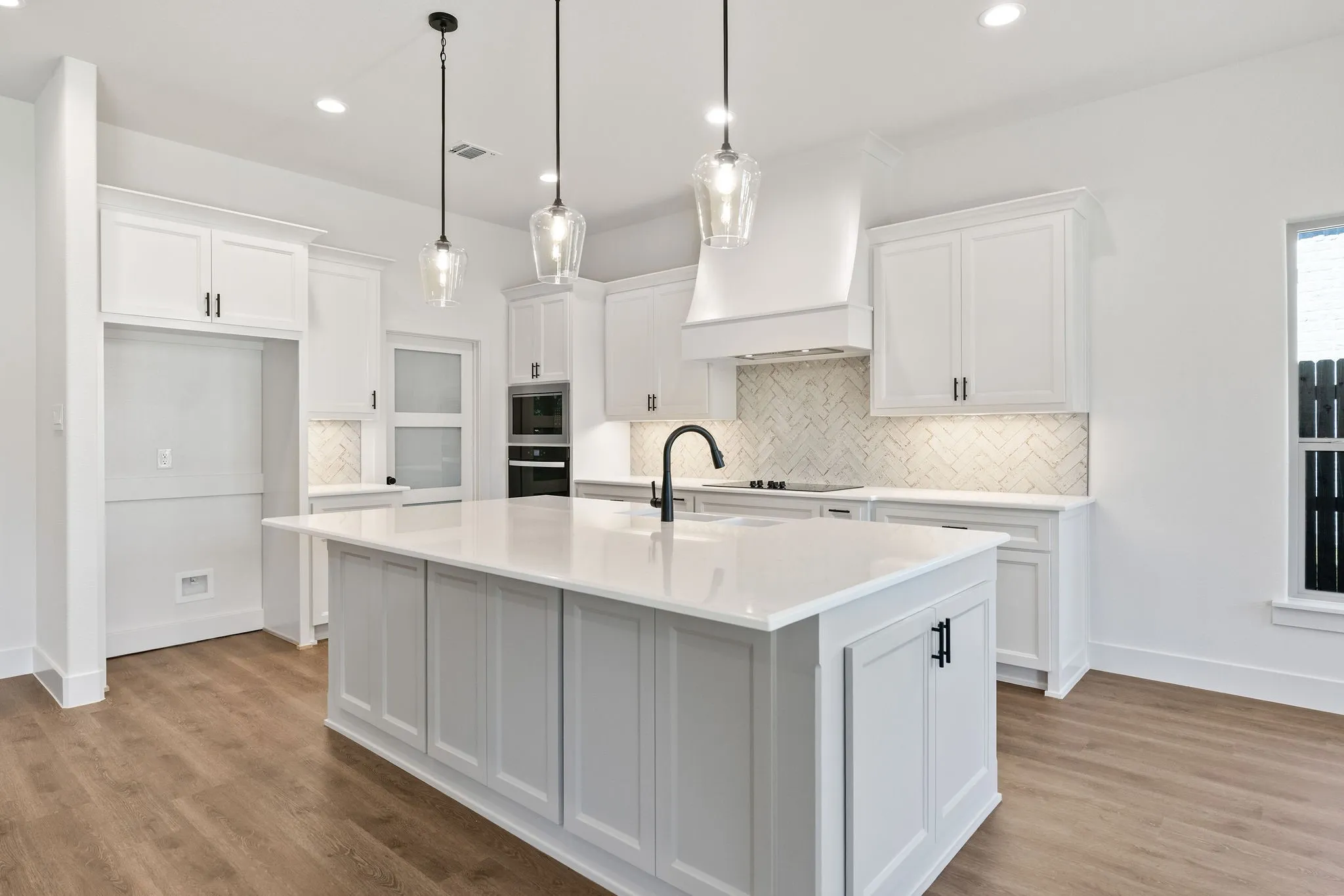 Kitchen featuring a central island with a solid surface countertop, white cabinetry with matte black hardware, integrated double ovens, and wood-finish flooring