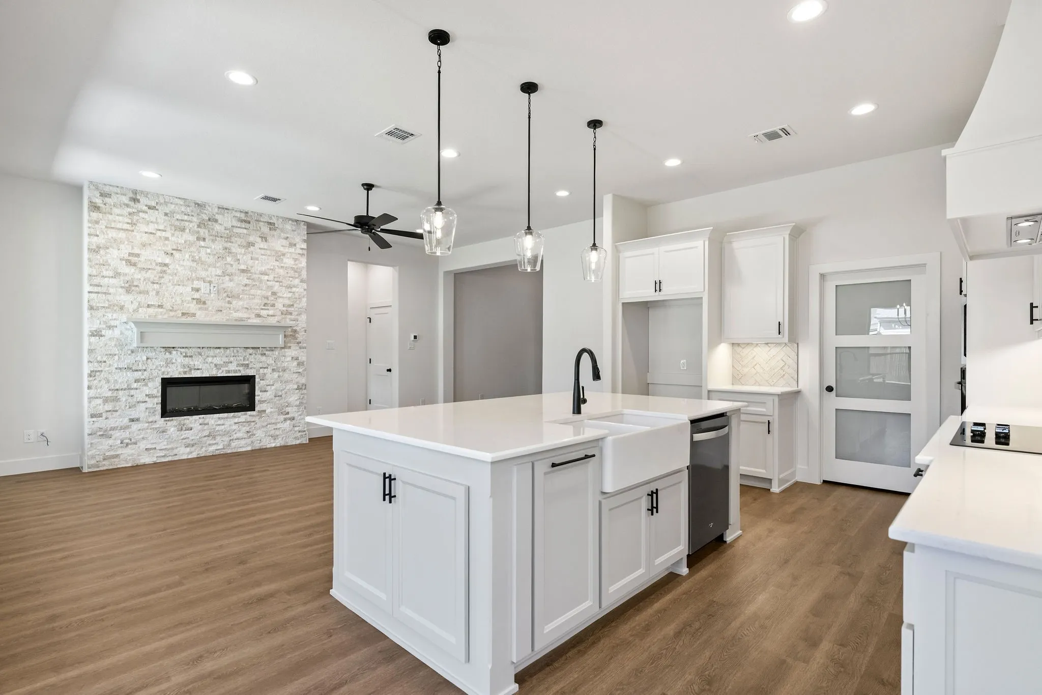 Open-concept living space featuring a central island with a farmhouse sink, white cabinetry, integrated cooktop, and an accent fireplace with a mantel
