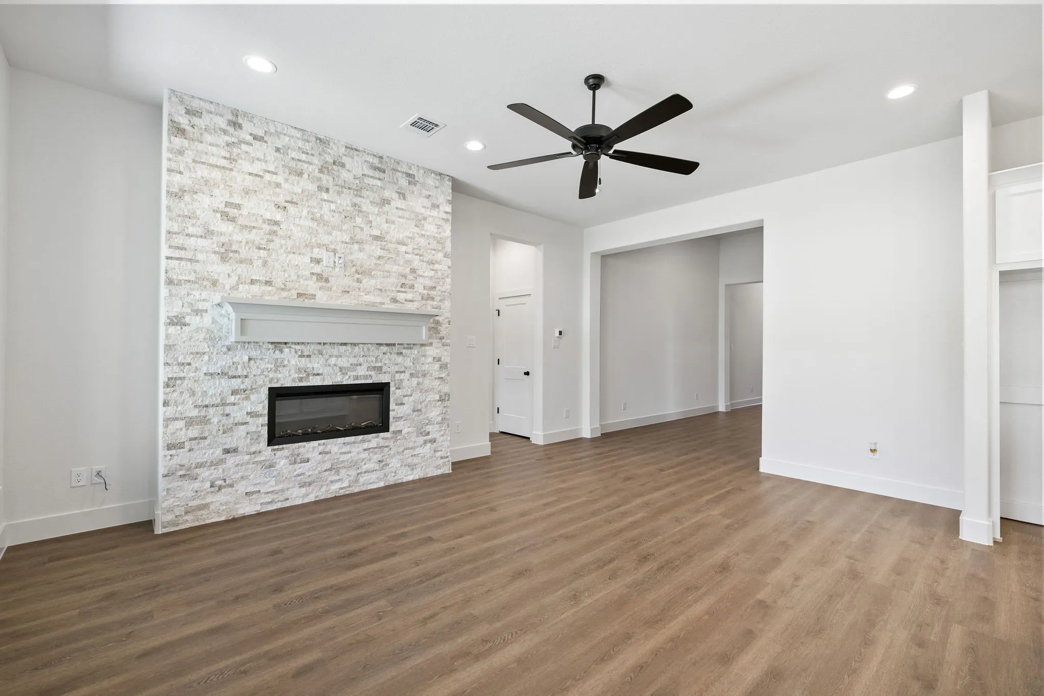 Spacious living area featuring a stone accent wall with a fireplace, wood-finish flooring, recessed lighting, a ceiling fan, and built-in shelving