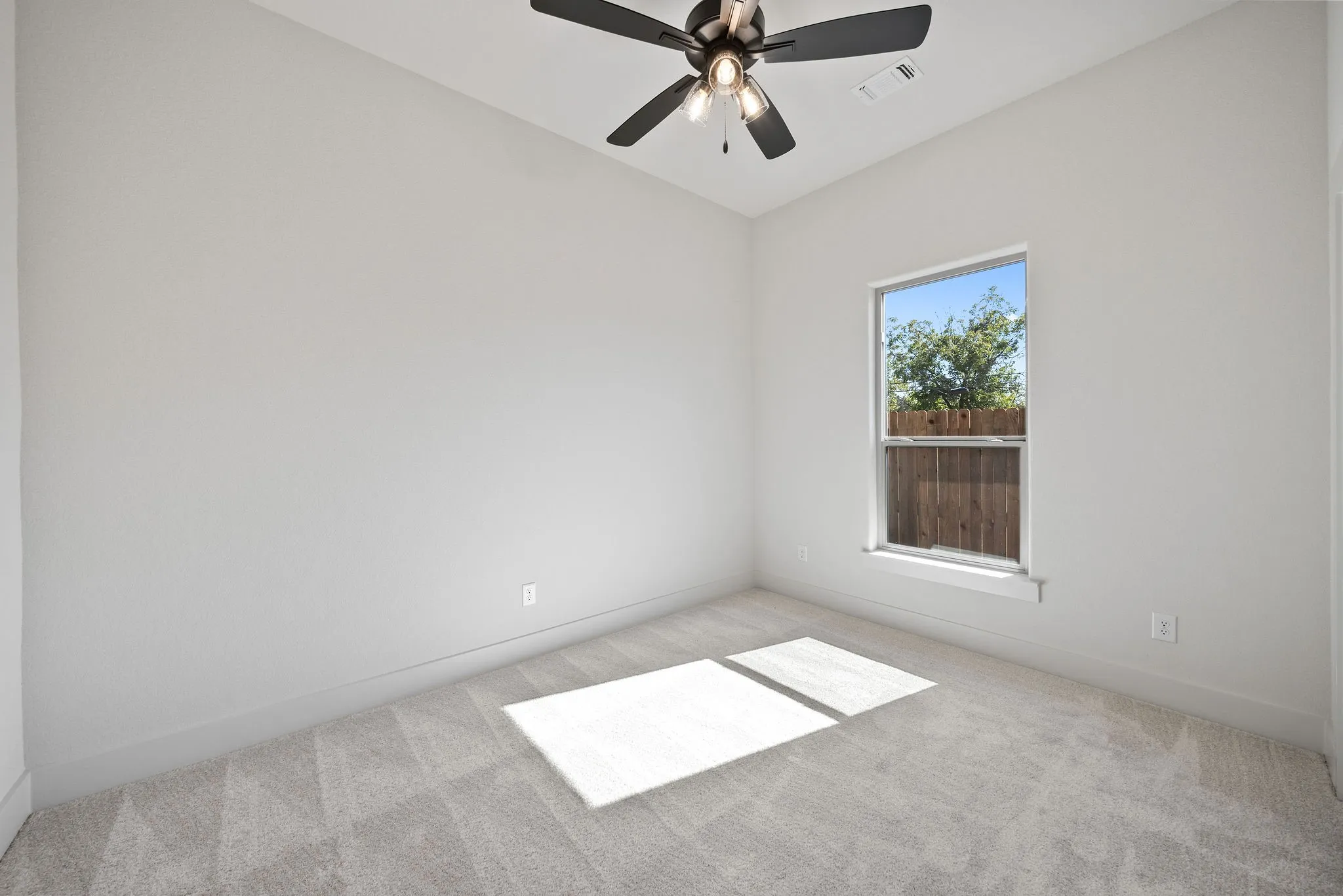 Neutral-toned room featuring a single window, light gray carpeting, and a ceiling fan with integrated lighting