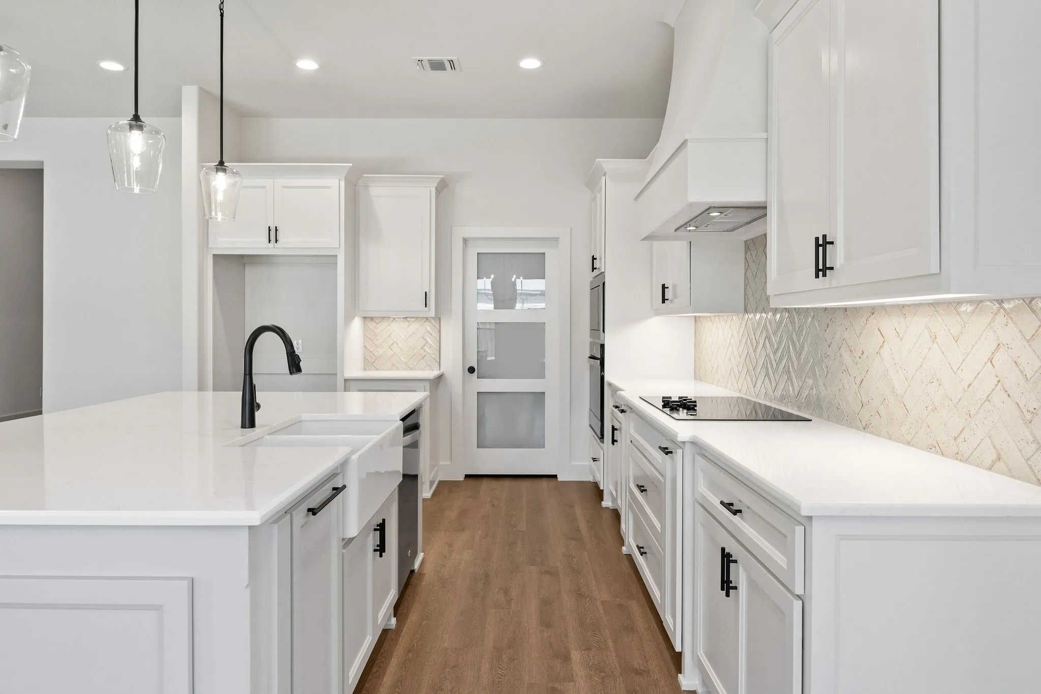 Modern kitchen featuring white cabinetry, quartz countertops, a farmhouse sink with a black matte faucet, a herringbone tile backsplash, and wood-finish flooring