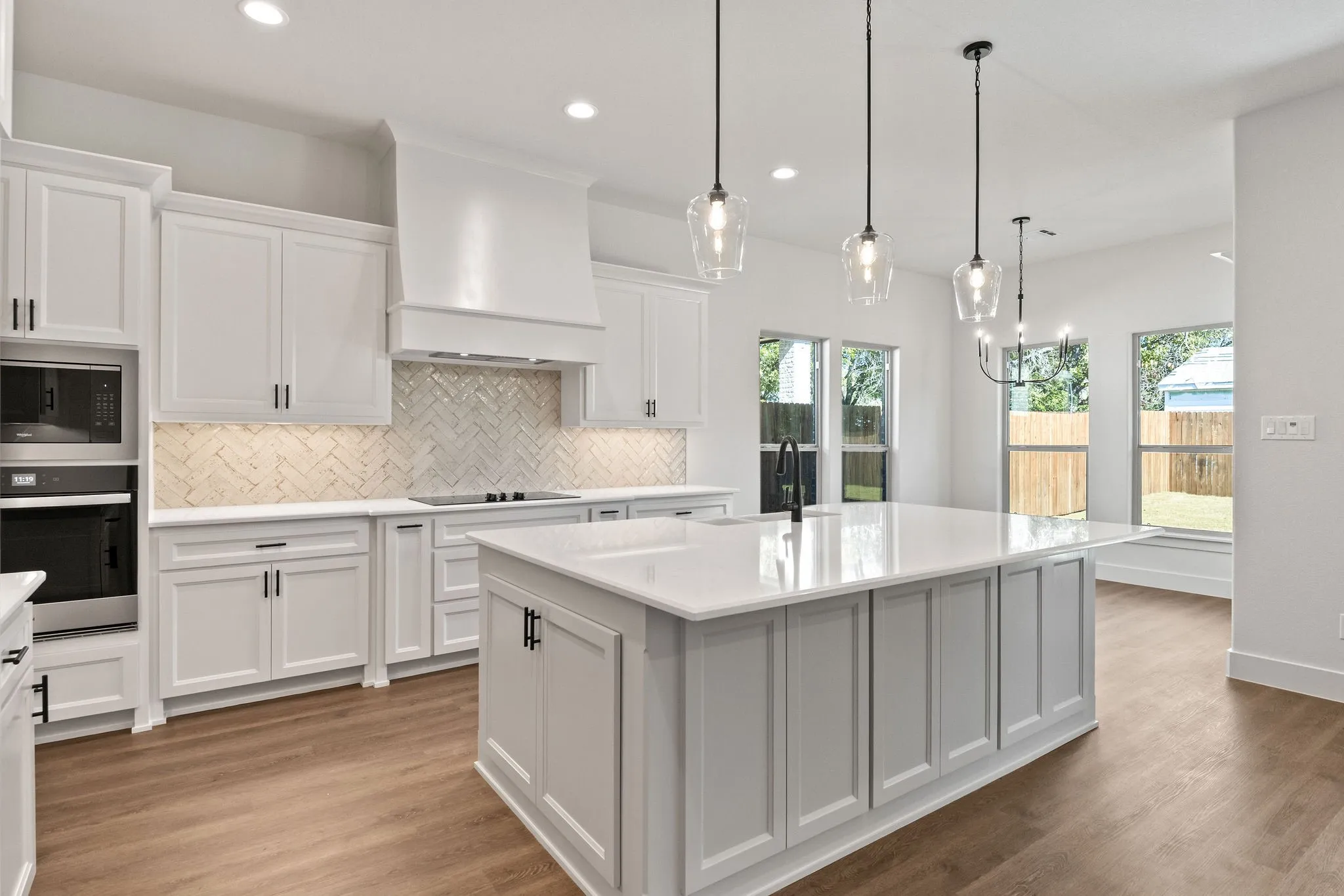 Modern kitchen featuring white shaker cabinetry, an expansive central island with a quartz countertop, stainless steel appliances, a herringbone tile backsplash, and wood-finish flooring