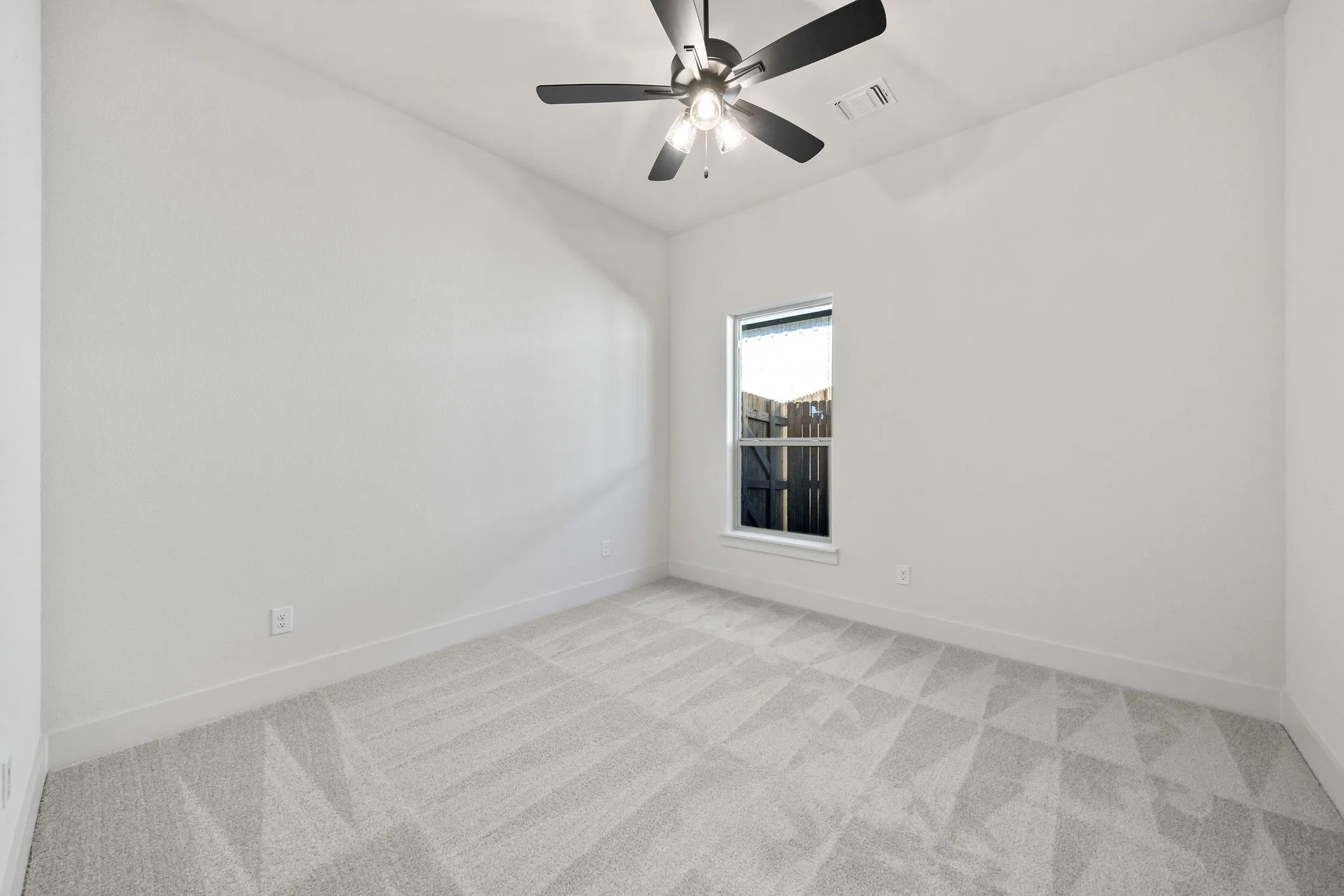 Room featuring light gray patterned carpeting, a single window, white walls, and a ceiling fan with integrated lighting