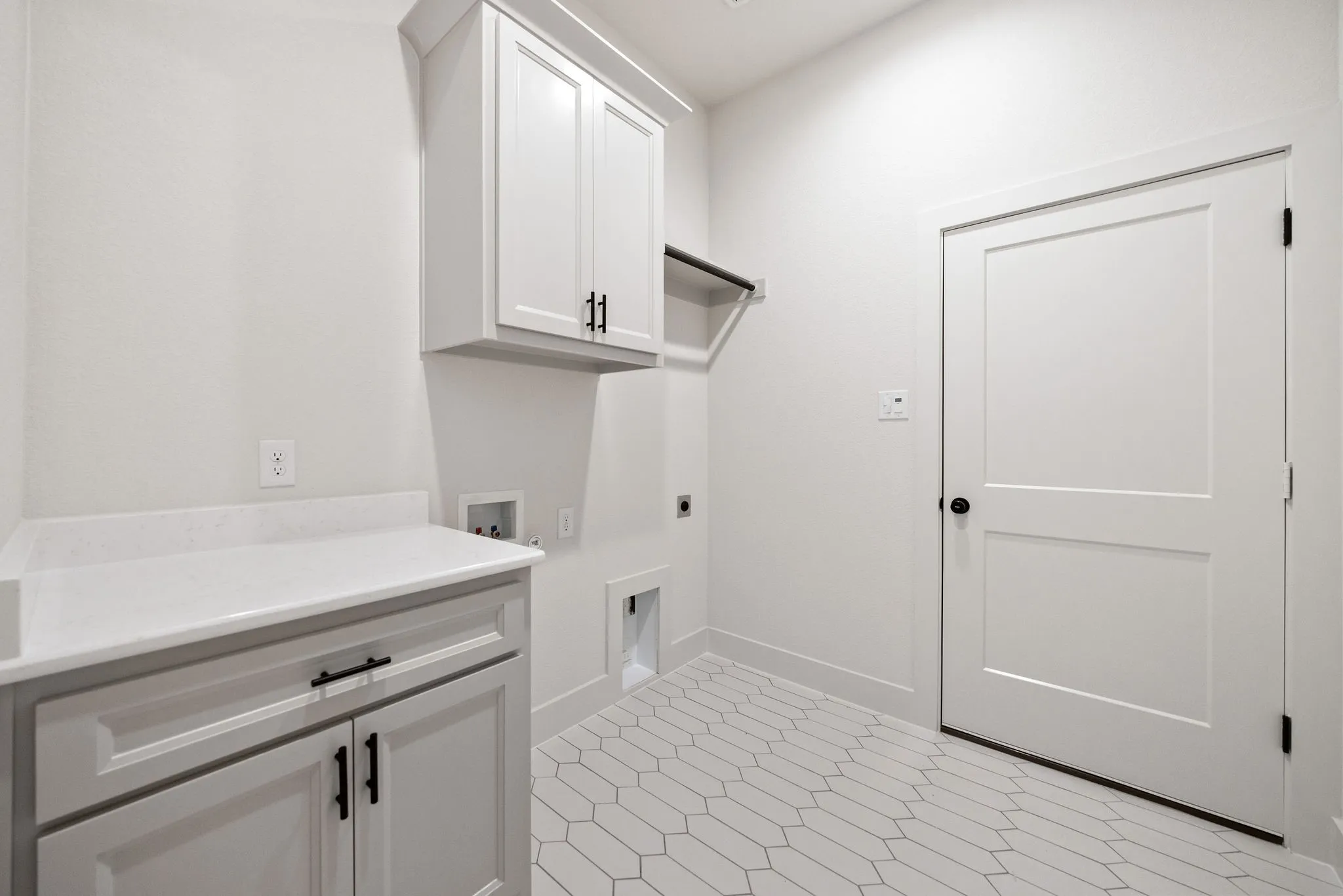 Laundry area featuring white cabinetry with black hardware, a light-toned countertop, a built-in hanging rod, and geometric tile flooring