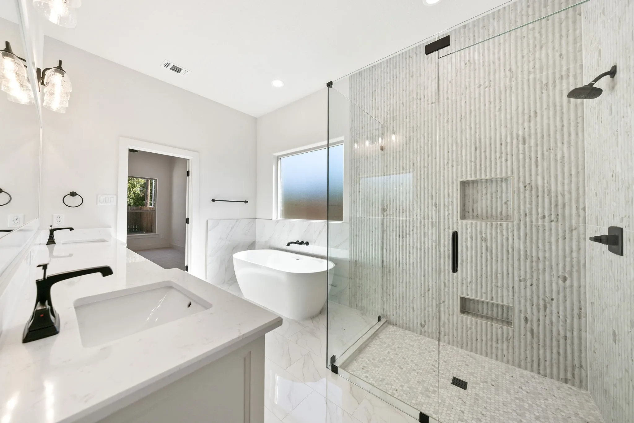 Contemporary bathroom featuring a frameless glass shower enclosure with textured tile walls and two recessed niches