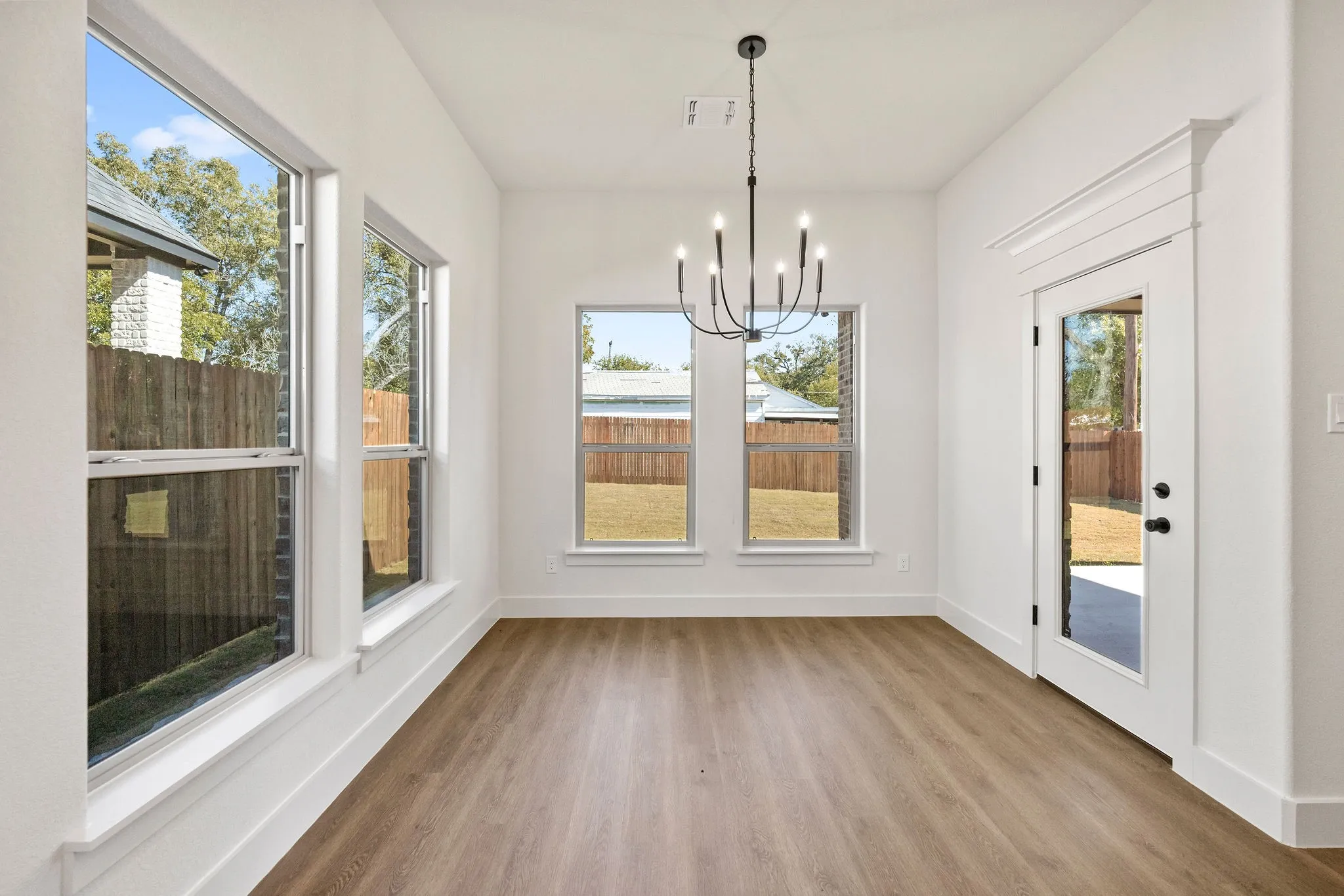 Bright interior space featuring wood-finish flooring, multiple windows, a ceiling-mounted chandelier, and a glass-paned door with decorative trim