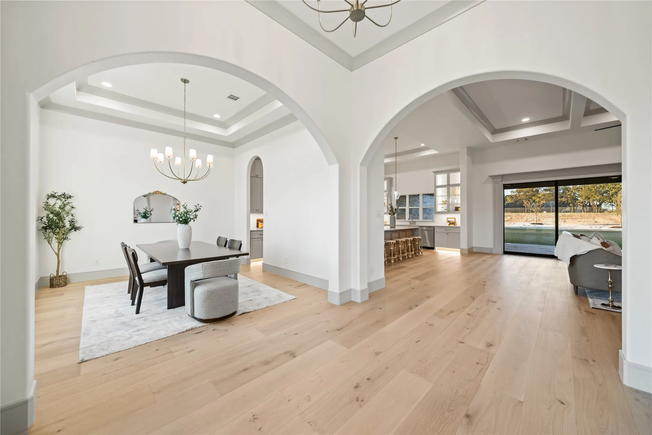 Expansive wood-finish flooring throughout, featuring a dining area with a tray ceiling and chandelier lighting