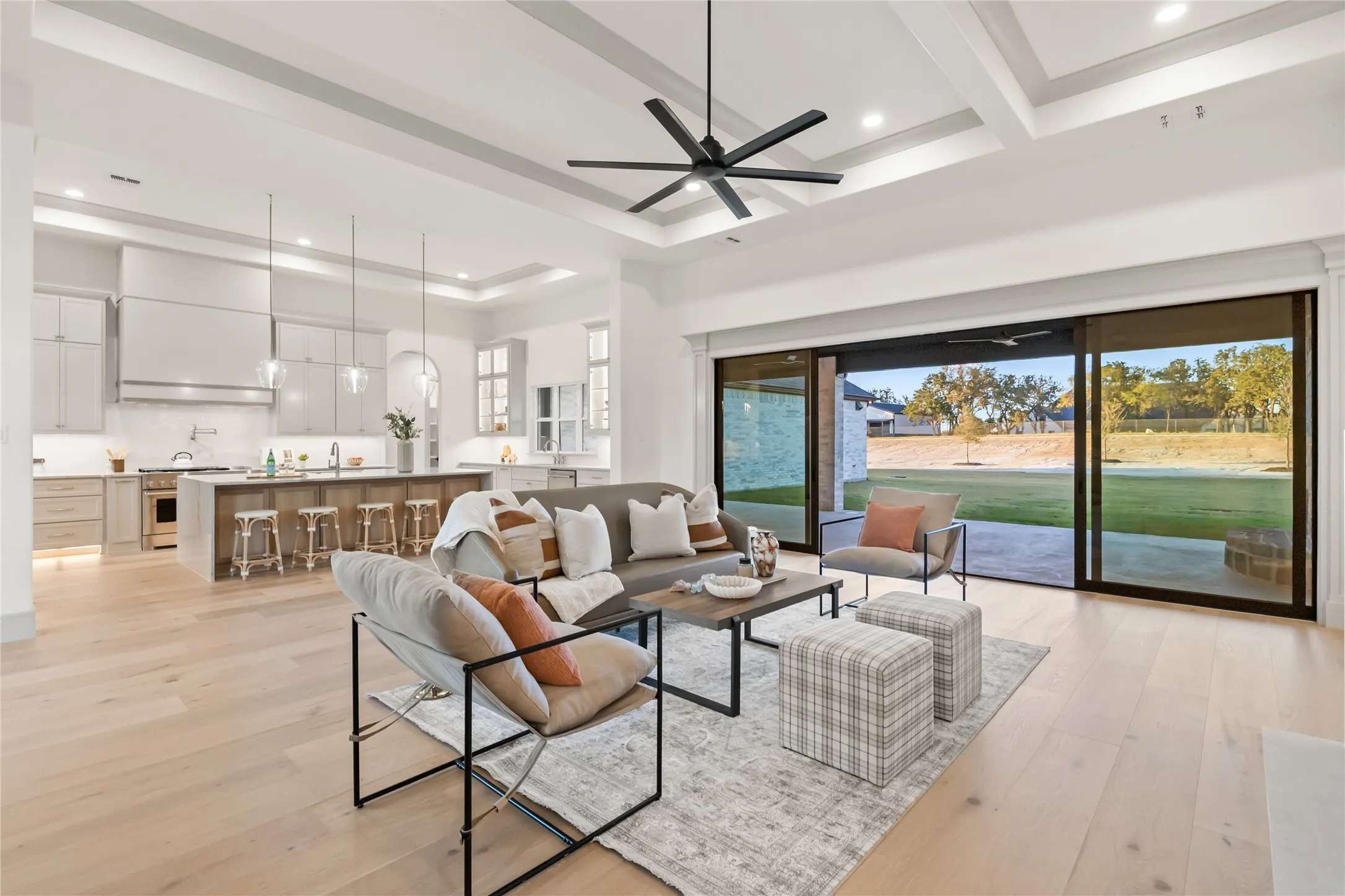 Expansive open-concept living area featuring light wood-finish flooring, a coffered ceiling, and a large multi-panel sliding glass door
