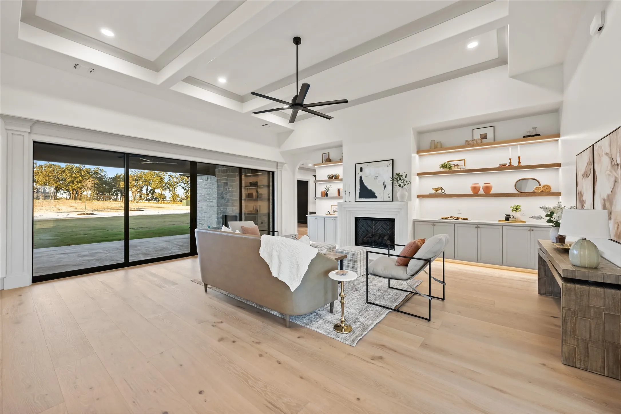 Spacious living area featuring light wood-finish flooring, a contemporary fireplace with mantel, and built-in shelving with integrated lighting