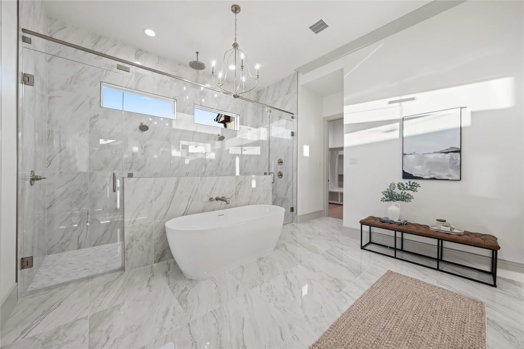 Spacious bathroom featuring a freestanding soaking tub, an expansive glass-enclosed shower with multiple showerheads, marble-patterned tile flooring, a coordinating marble-patterned shower surround, and a contemporary chandelier