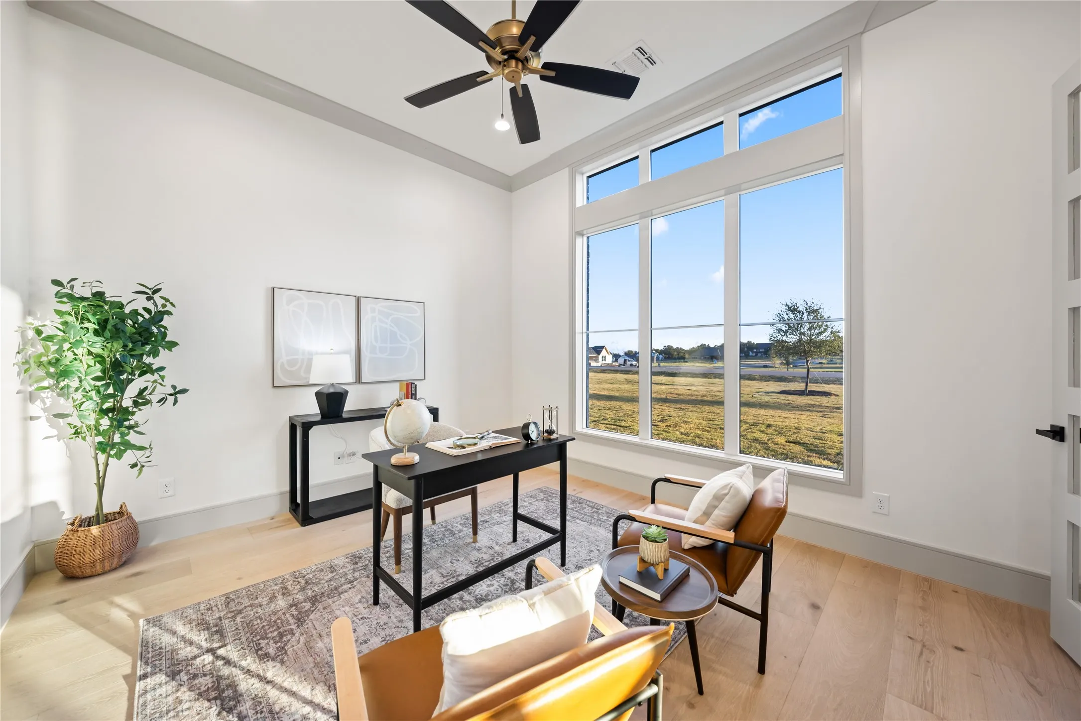 Spacious room featuring tall ceilings, light wood-finish flooring, and a contemporary ceiling fan