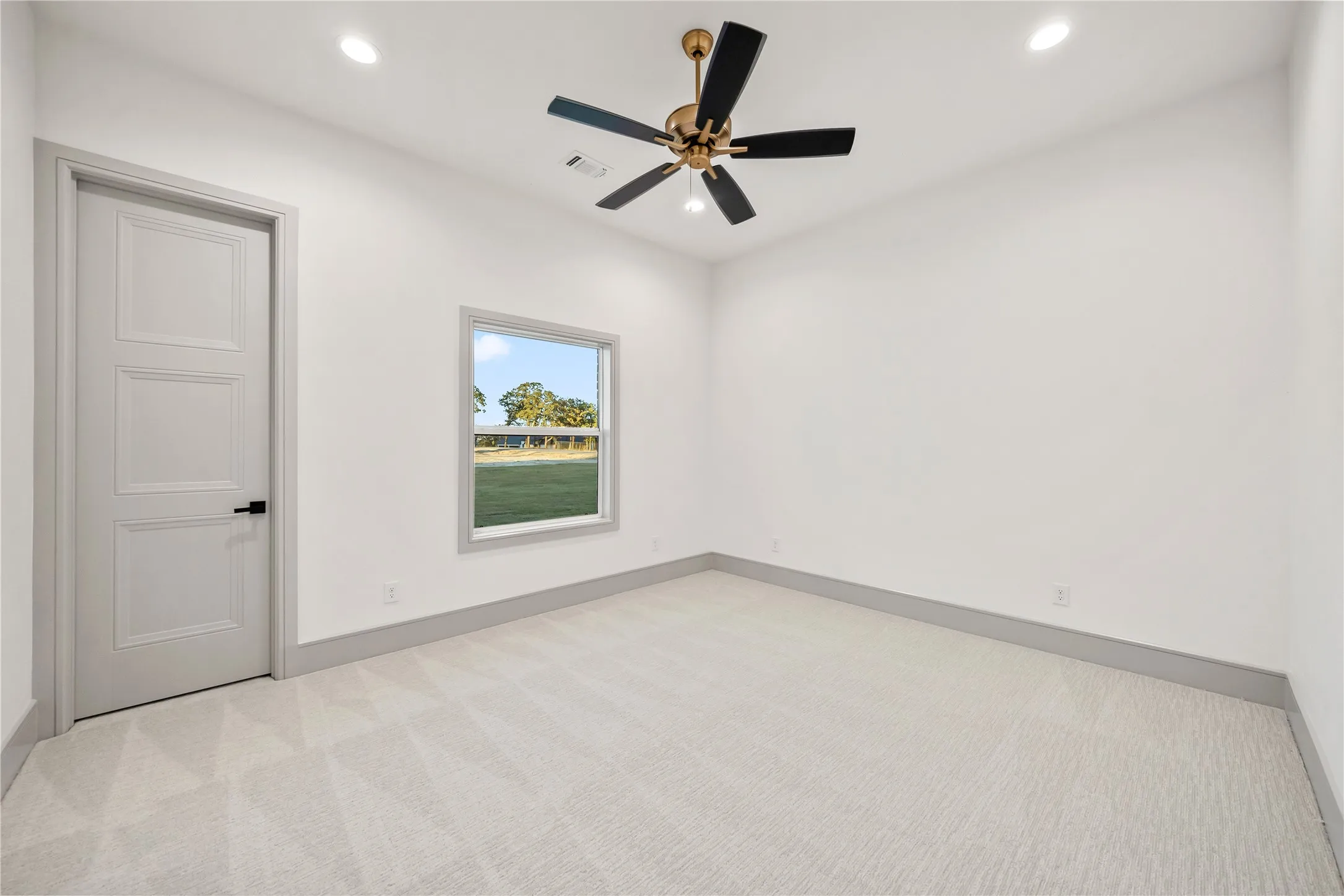 Spacious room featuring light-toned carpet, white walls, and a modern ceiling fan with bronze accents