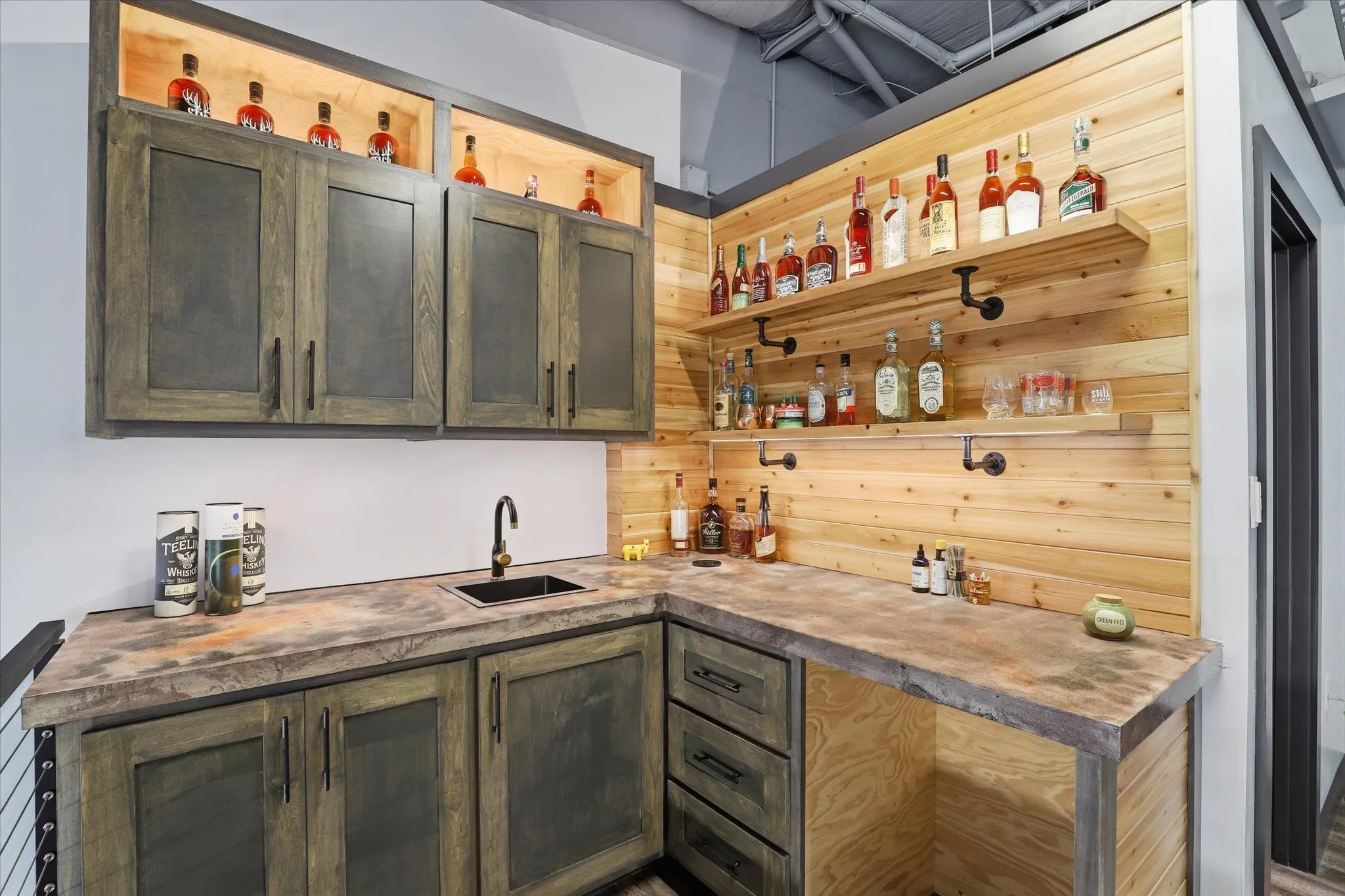 Custom bar area featuring built-in cabinetry, concrete-finish countertops, and a stainless steel sink with a matte black faucet