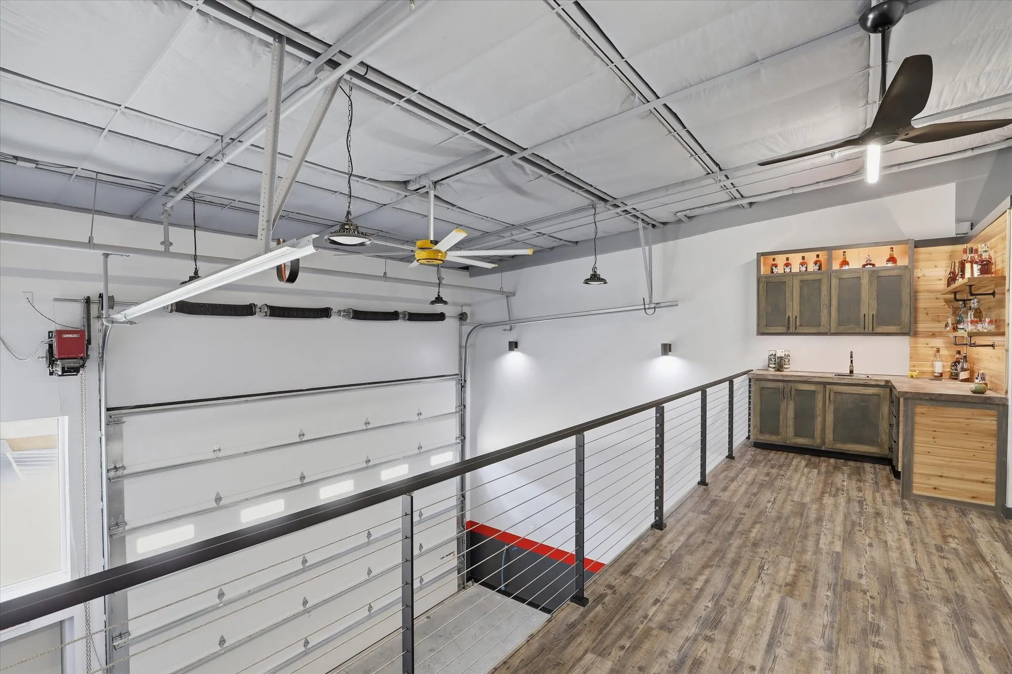 Upper-level entertainment area featuring wood-finish flooring, a built-in wet bar with distressed cabinetry, open shelving, and a cable railing system
