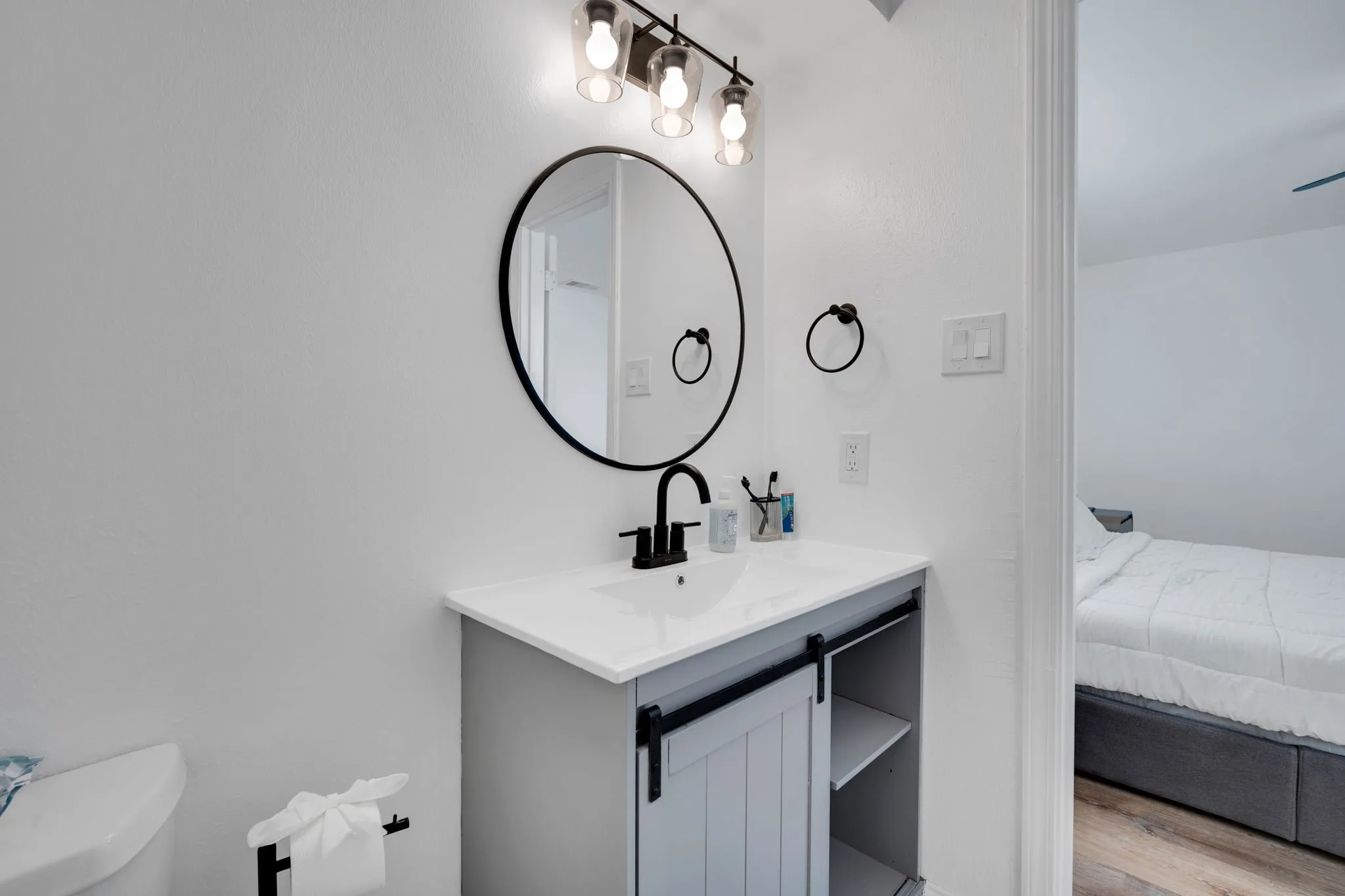 Bathroom vanity featuring a single basin sink with black hardware, a round framed mirror, and a three-light fixture