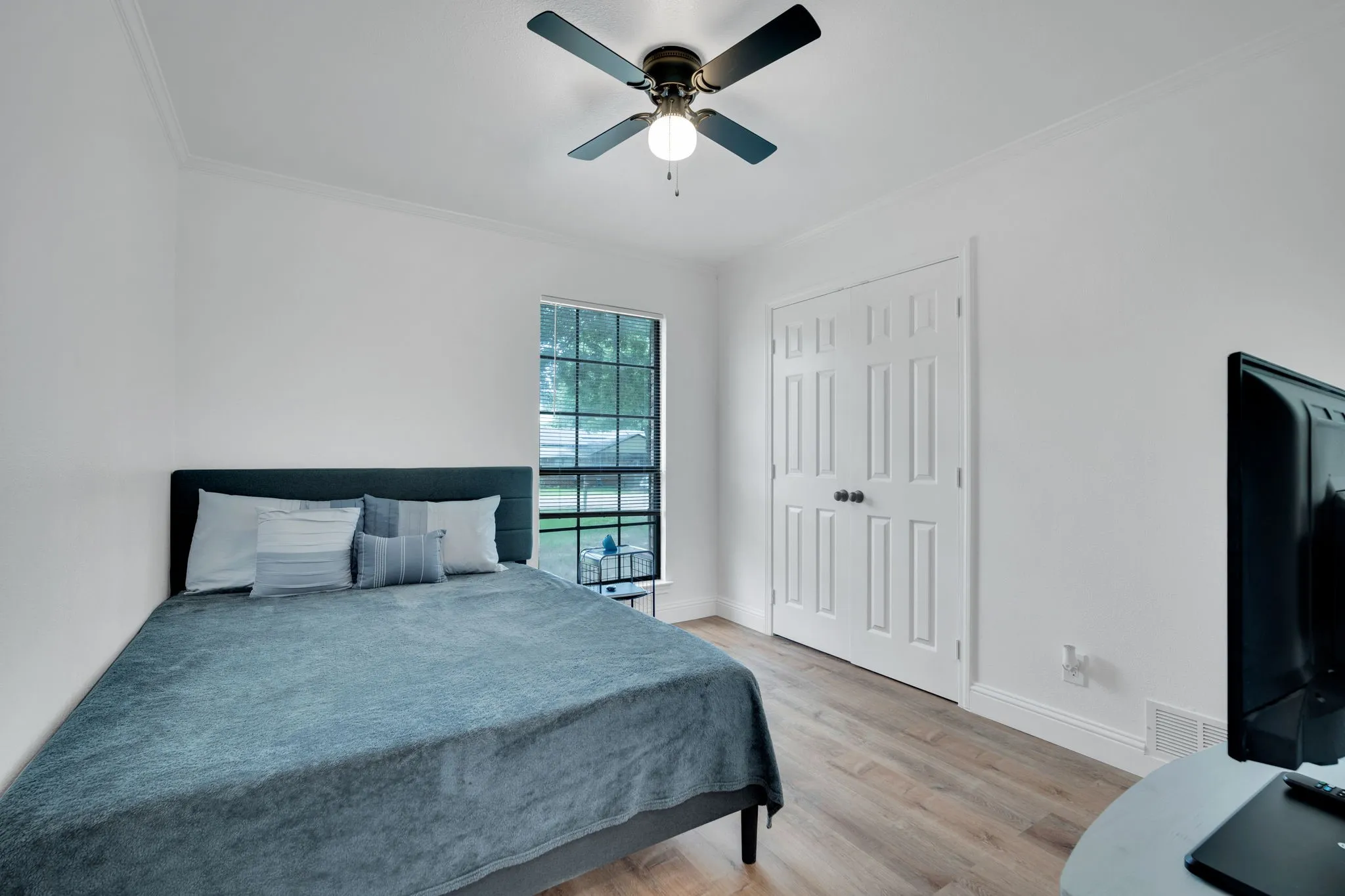 Bedroom featuring a ceiling fan, crown molding, double-panel bifold closet doors, a large window, and wood-finish flooring